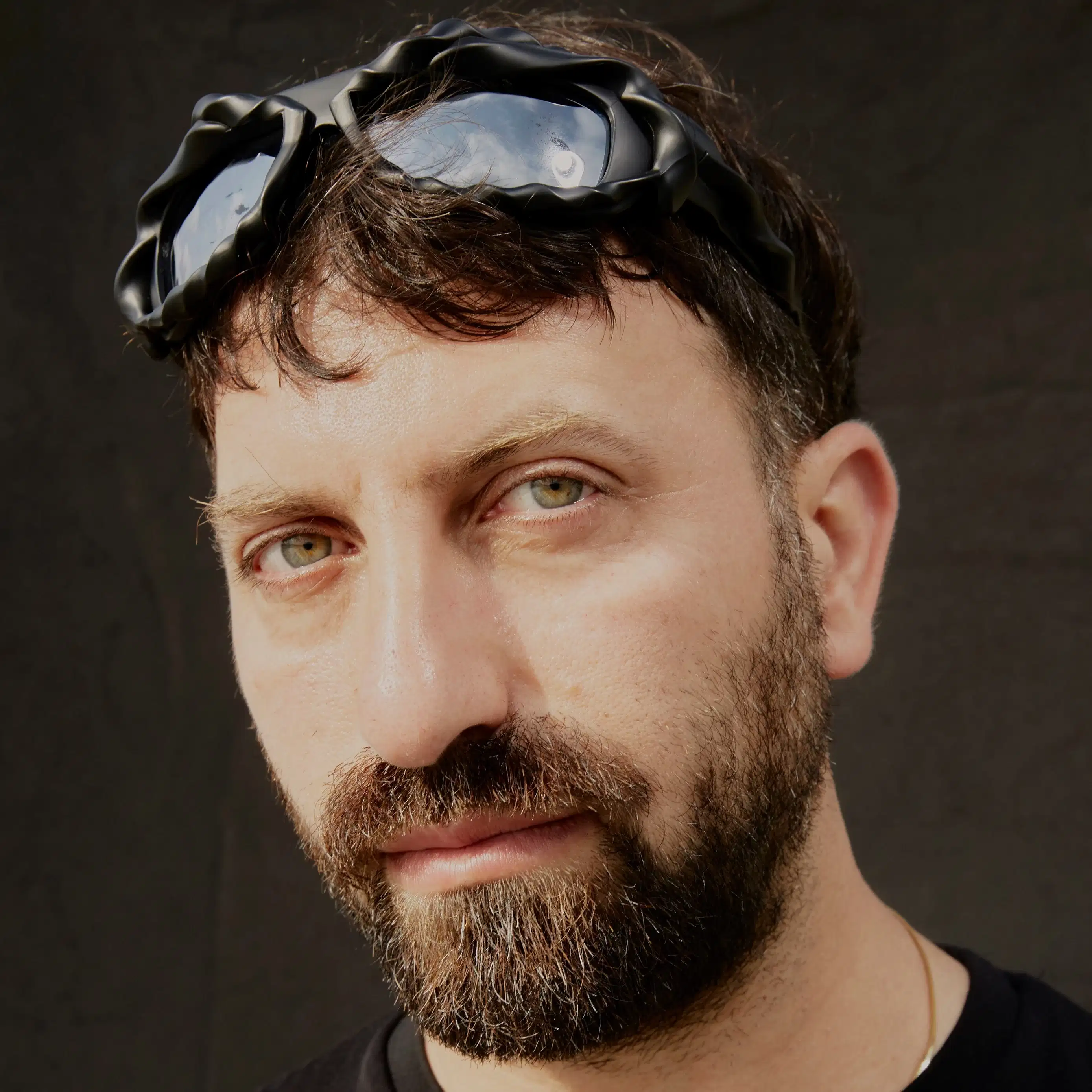 a person with a brown beard, bleached eyebrows and green eyes stares at the camera