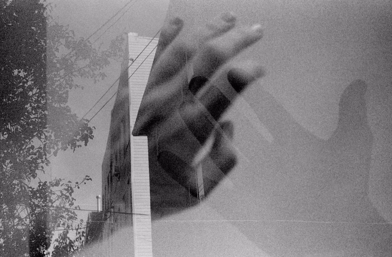 Black and white photo of two hands transposed over an apartment building with trees and power lines.