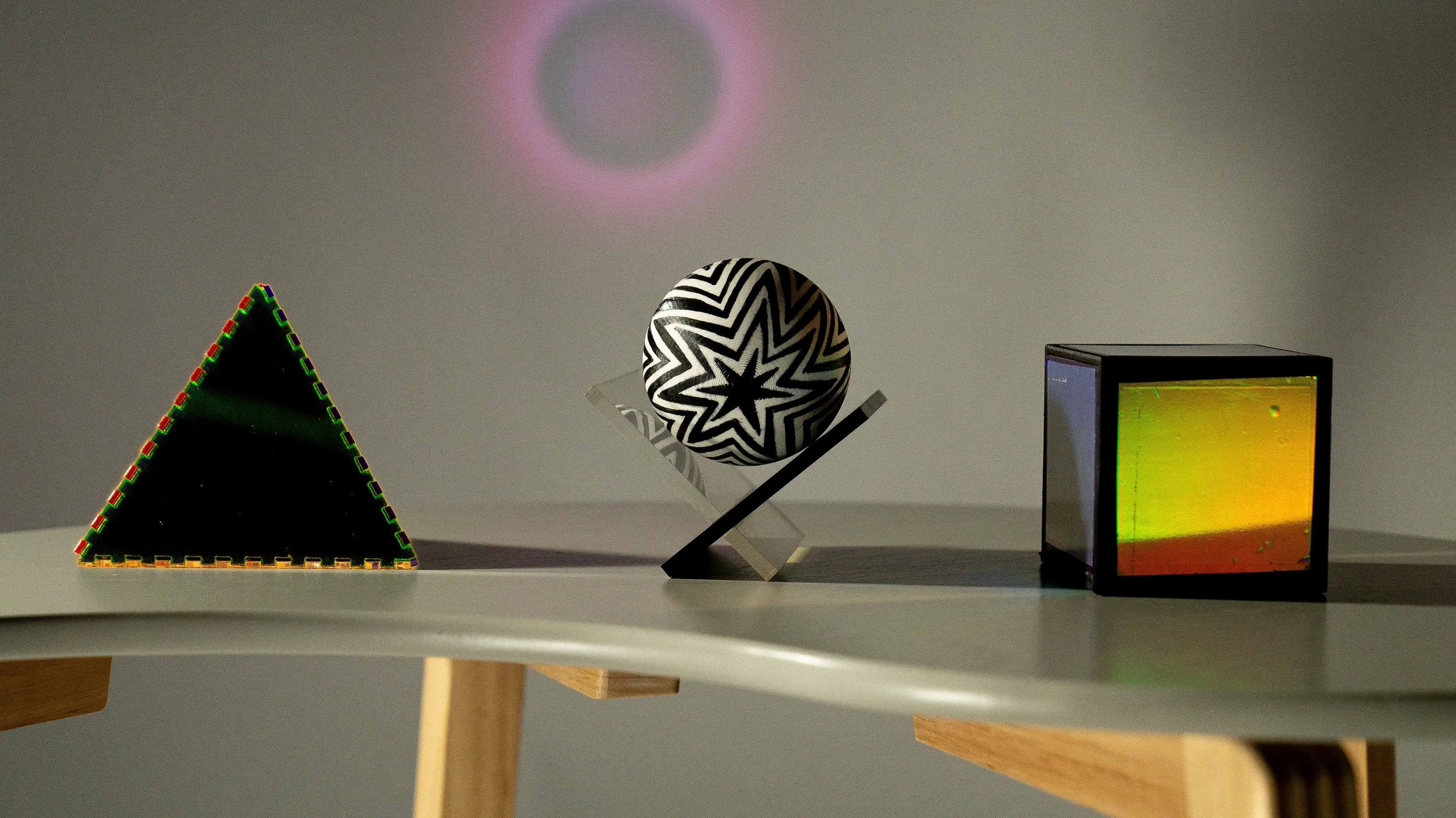 3 Plastic, 3D Objects sit atop a table with the shape of a circular light in the background. 