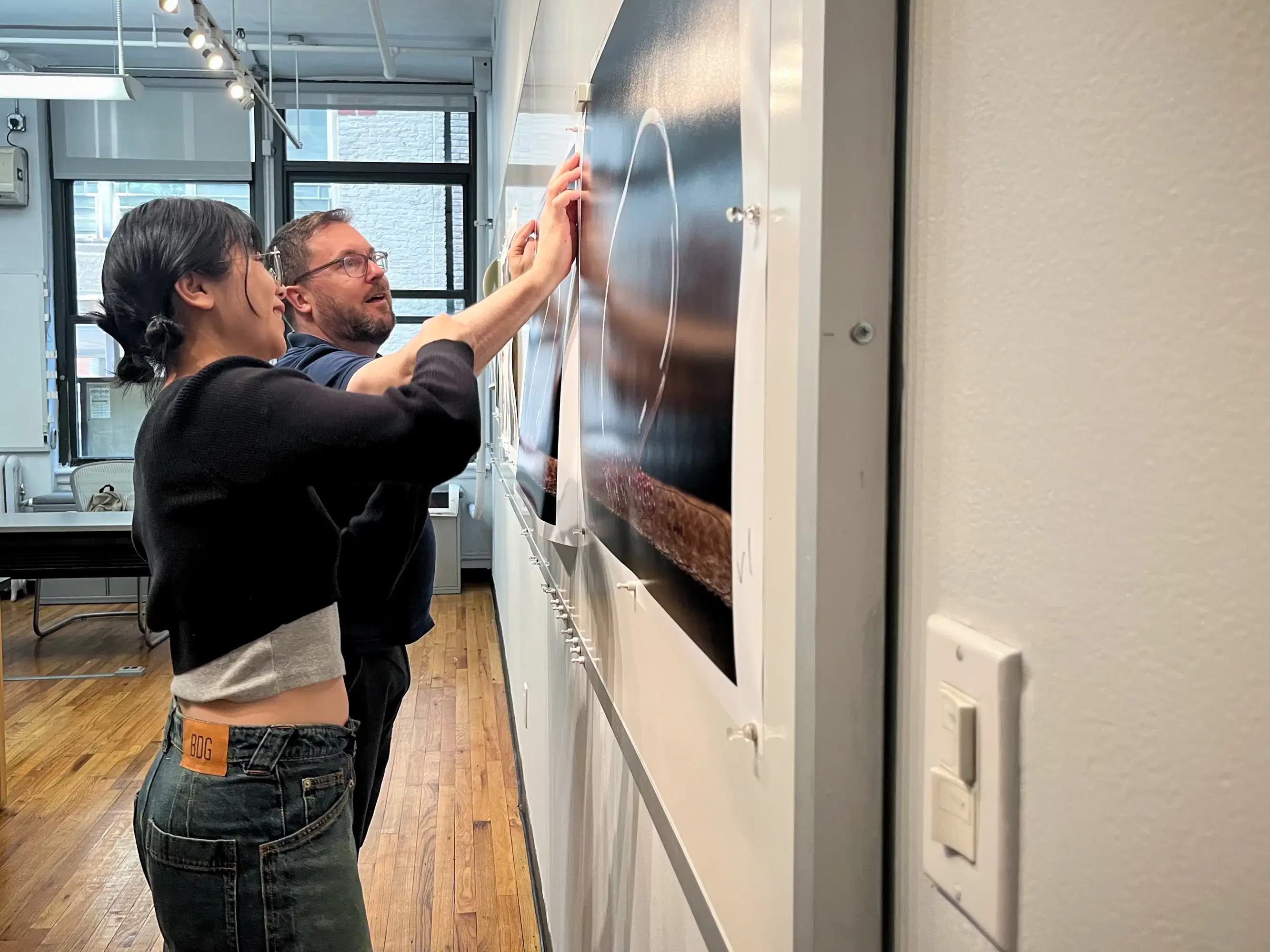 a student and professor examine a photo print that hangs on a wall.
