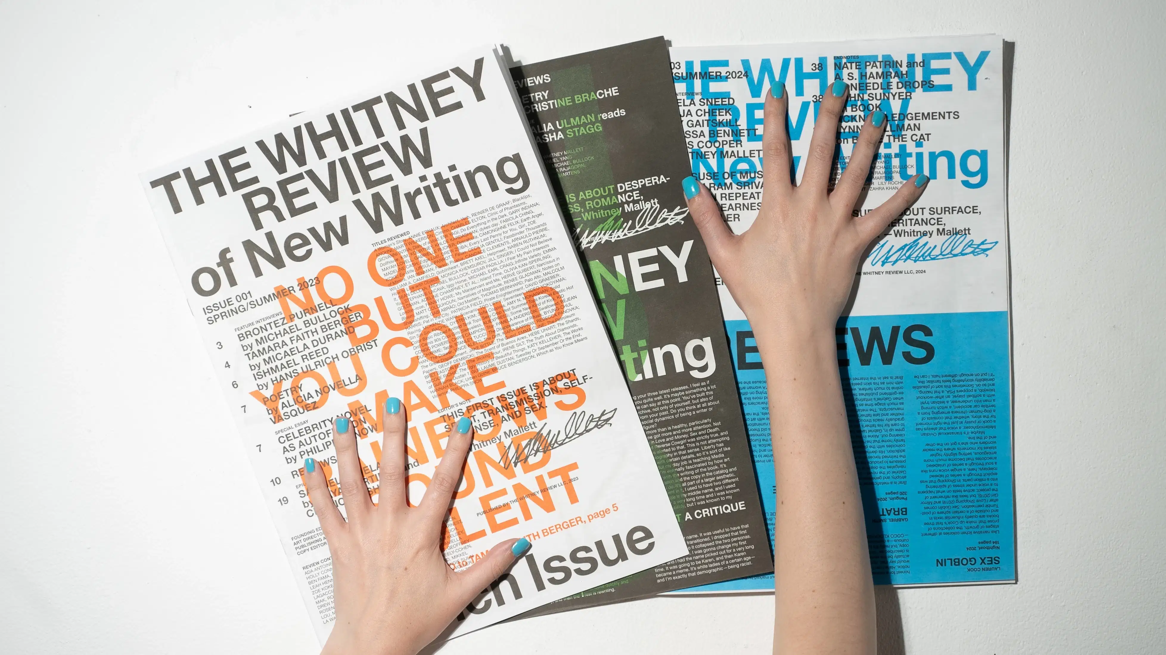 Issues of The Whitney Review with hands on top of them