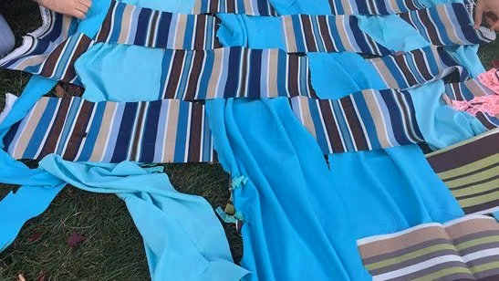 Blue quilt being down outside in the grass.