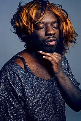 an african american male with female cloths and a wig.