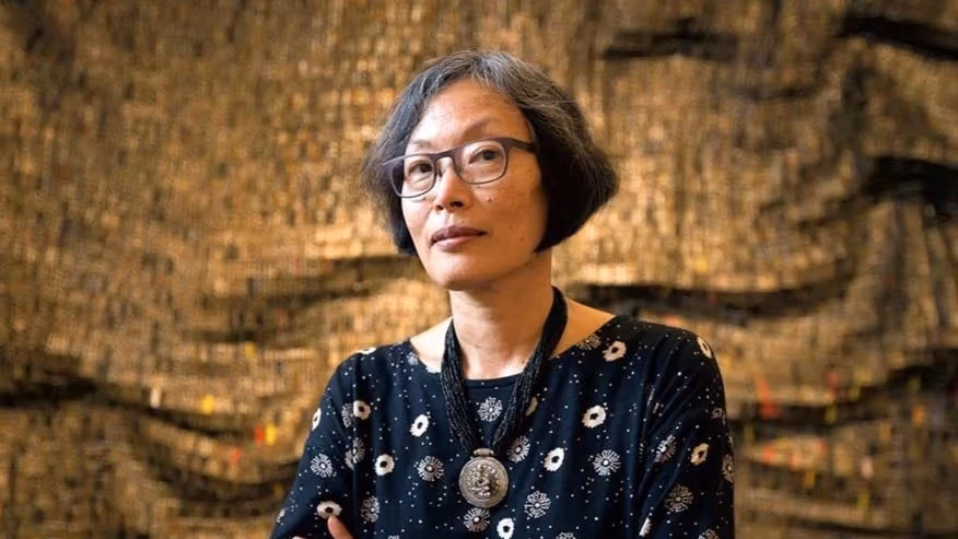 Portrait of woman with short cropped hair and glasses in front of bronze background.
