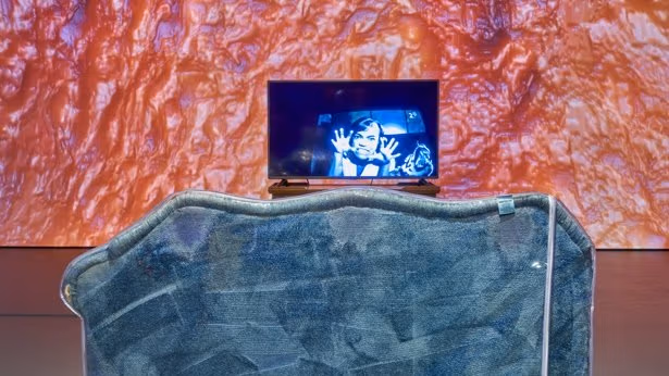 A TV screen displays a person making an expression, with her hands by her face.