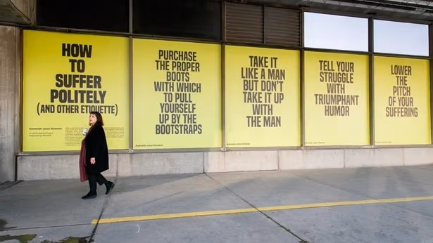 A woman walks down the sidewalk alongside yellow and black posters containing sayings of advice.