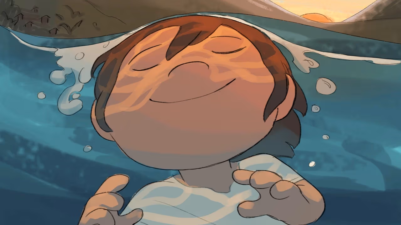 A boy smiles as water washes over him, the orange light from the setting sun illuminating his face.