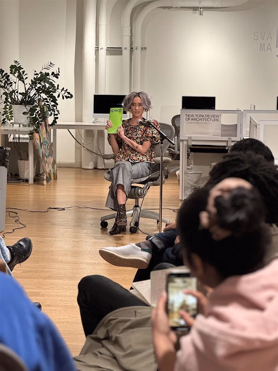 a person with gray hair holds up a book in front of a room of event attendees