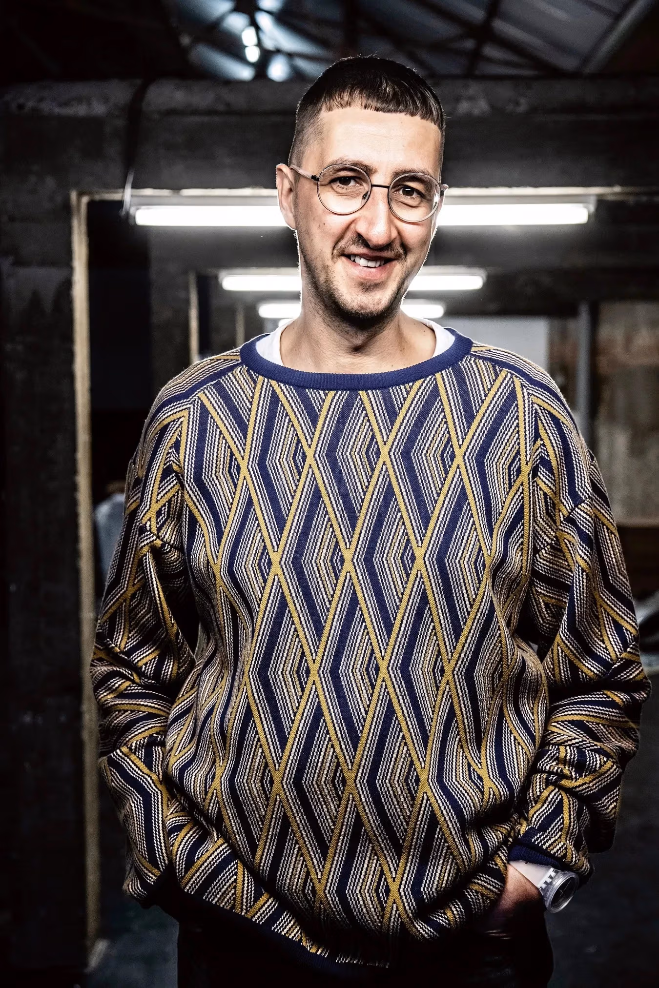 Image of Niels Van Tomme, a man in a blue and yellow diamond pattern sweater with his hands in his pockets