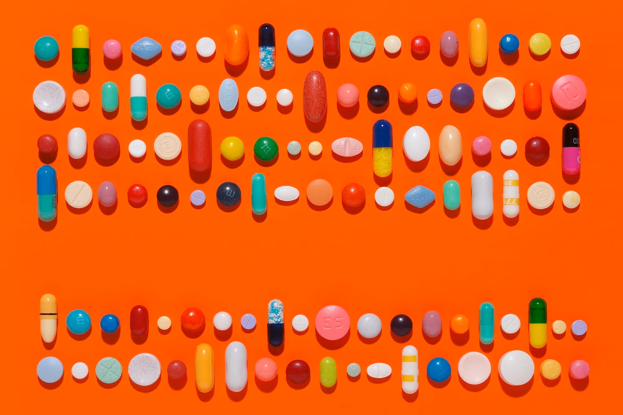 Capsules and pills in a linear composition on a bright orange background.
