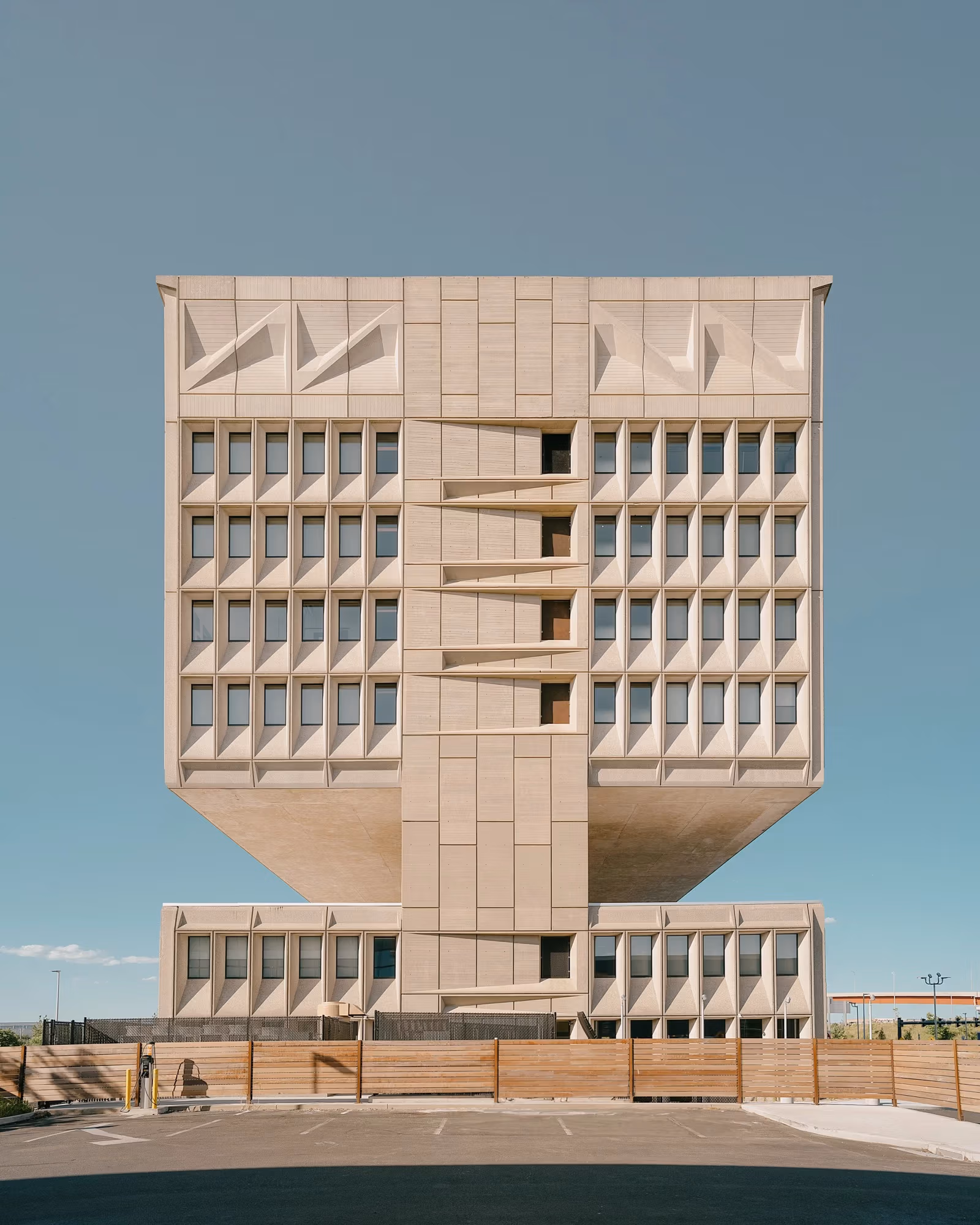 architectural color photo of a large square concrete building against a blue sky.