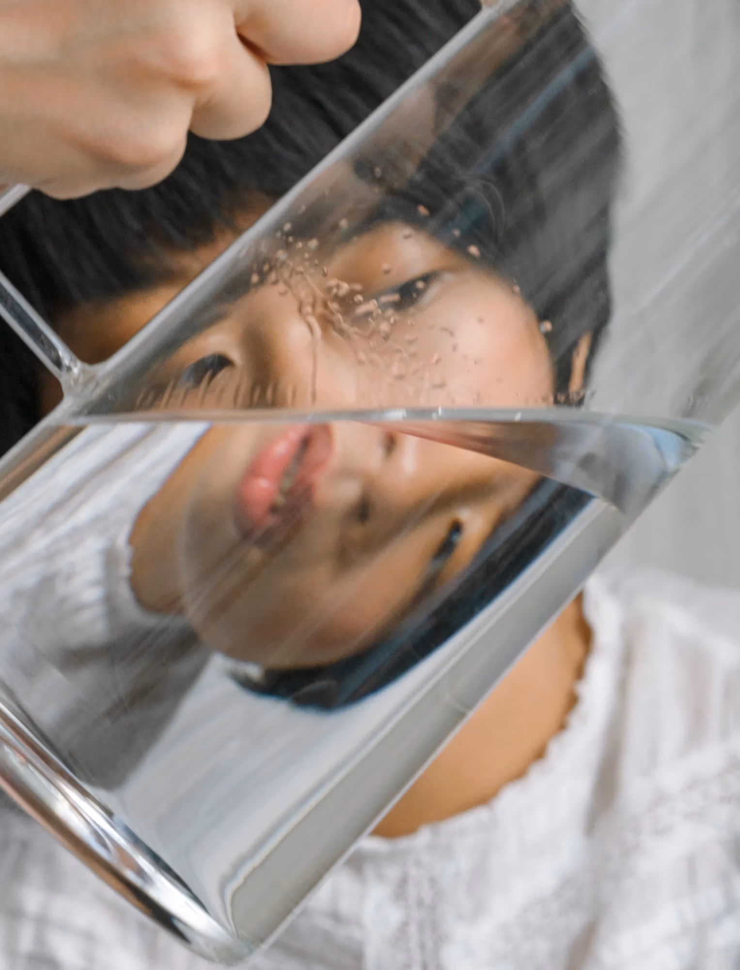 Self-portrait of a woman photographed through a half-empty pitcher, distorting the face.