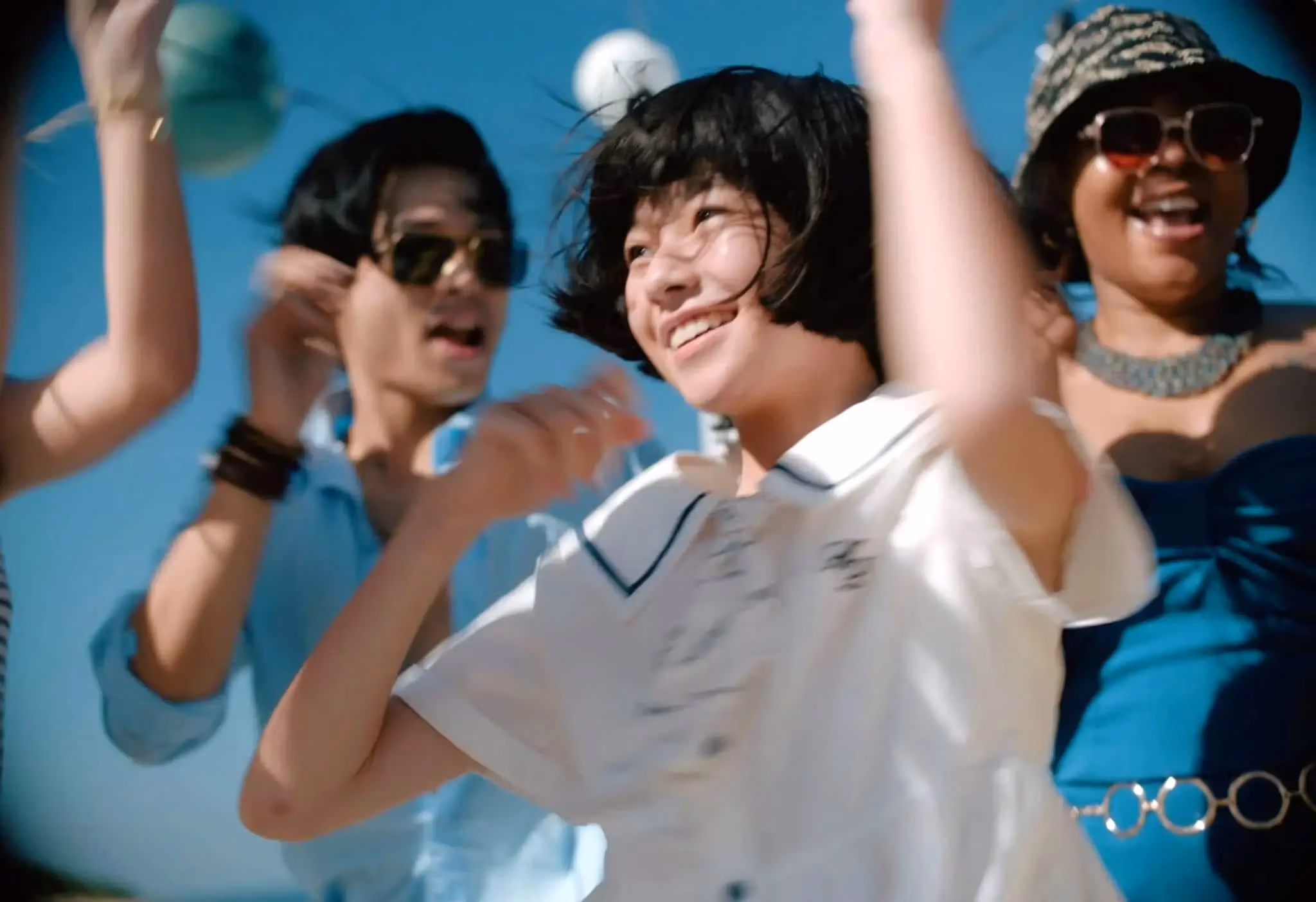 A joyful group of people dancing and smiling together under the bright sun.