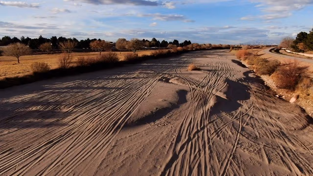 A dry, beige river bed landscape stretching to the horizon with a blue sky of the Rio Grande 