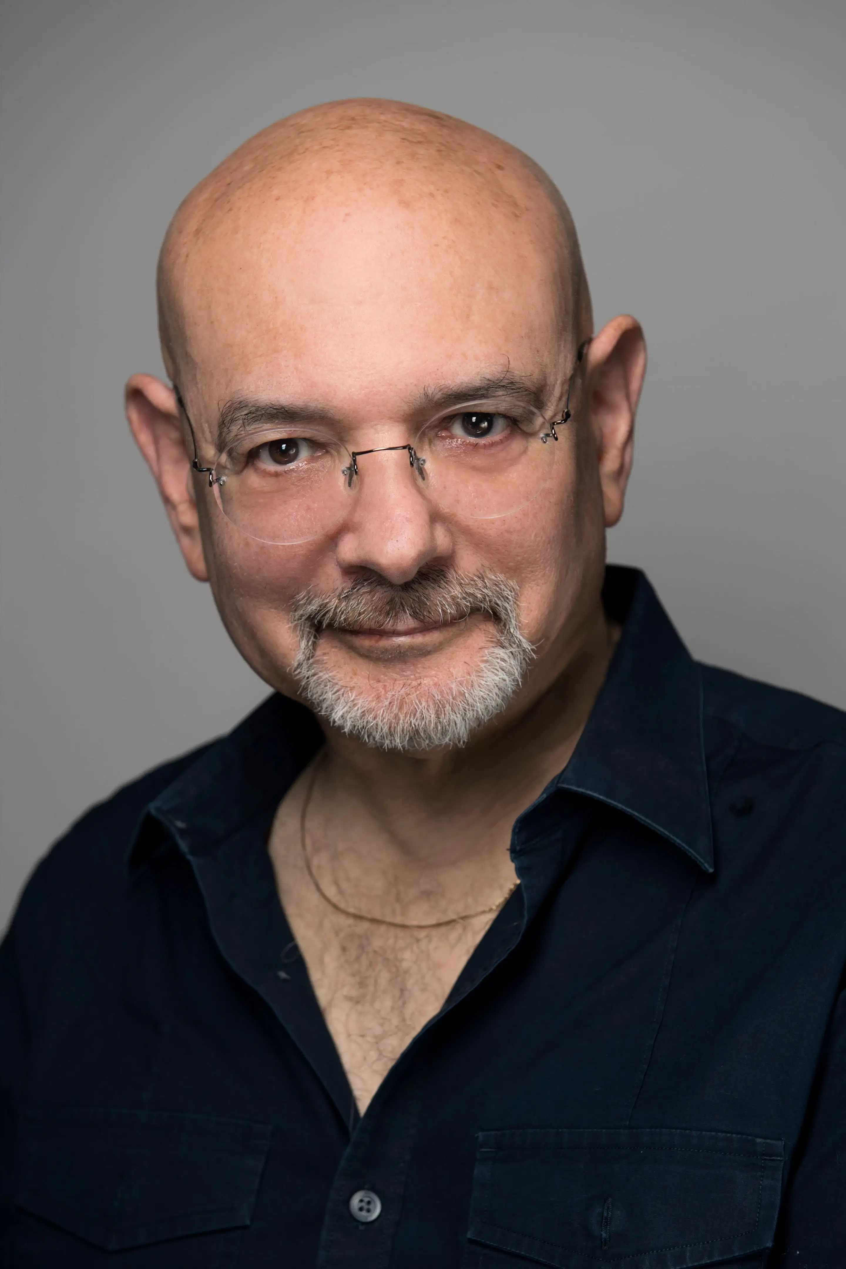 A white man with glasses and a goatee, wearing a dark shirt, poses against a plain background.