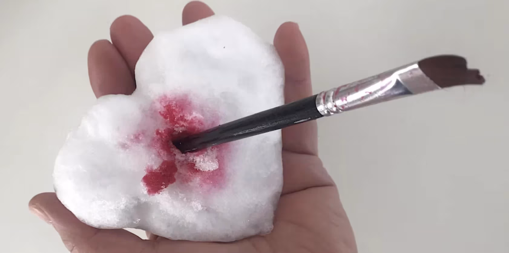 Peter Hristoff's hand with a snow heart pierced with a paint brush and red paint