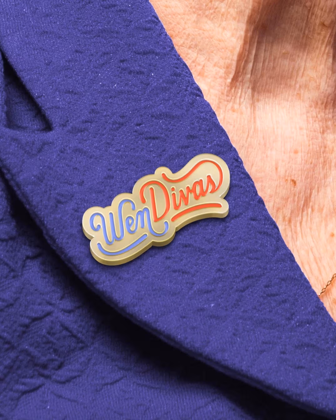 A woman wearing a purple dress with a custom made pin that reads "Wen Divas" pinned to it.