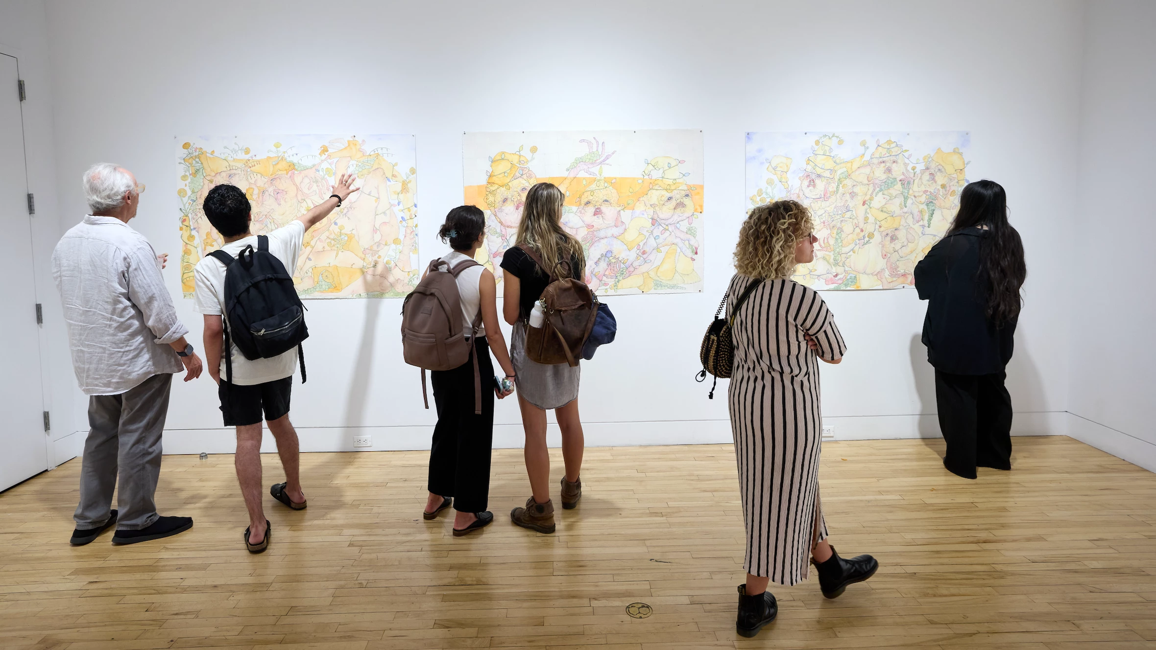 People in gallery look at three drawings on wall