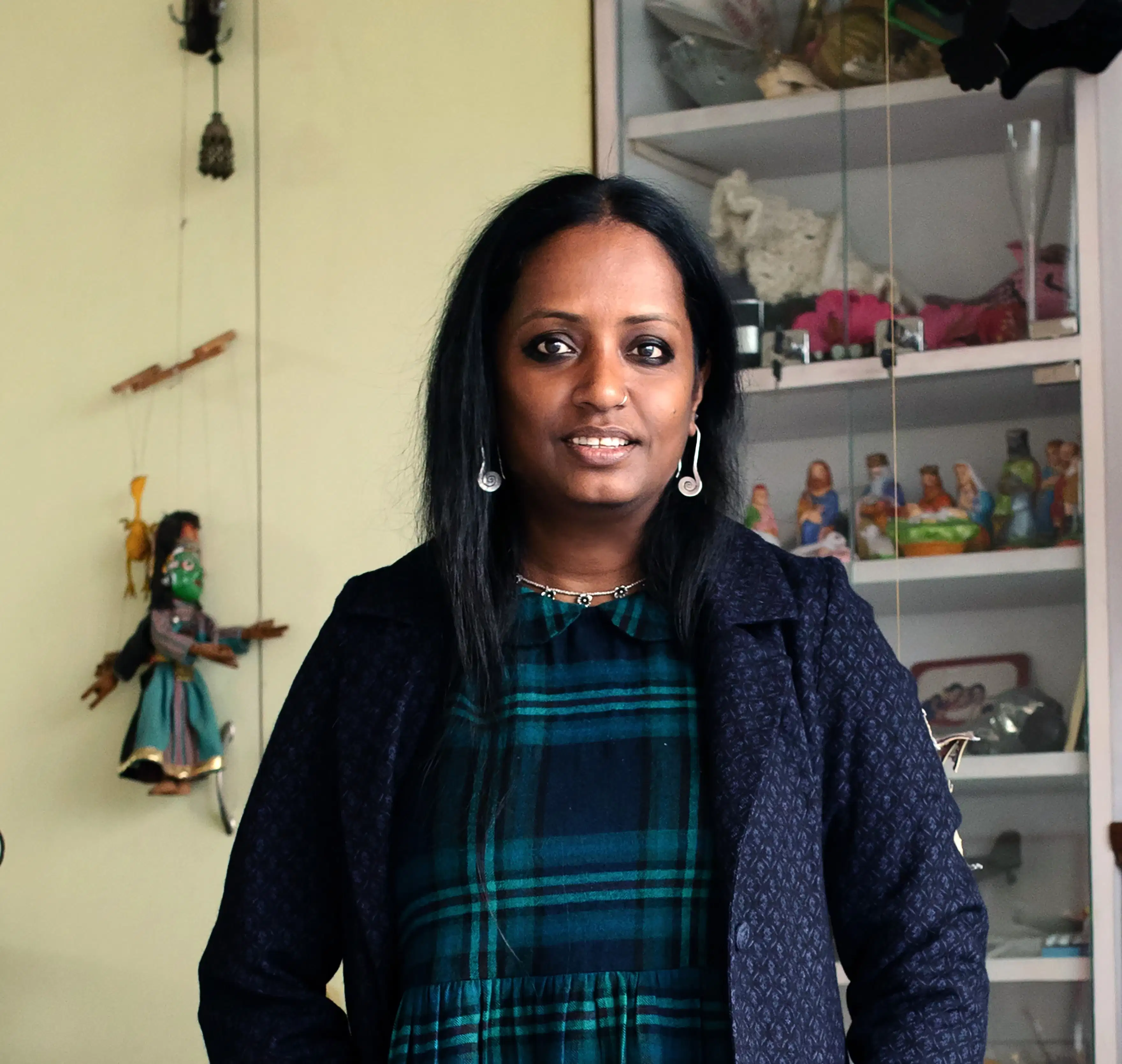 A photograph of Mithu Sen. Mithu is standing int he center of the photo and is wearing a blue and green plaid shirt with a davy blue jacket.