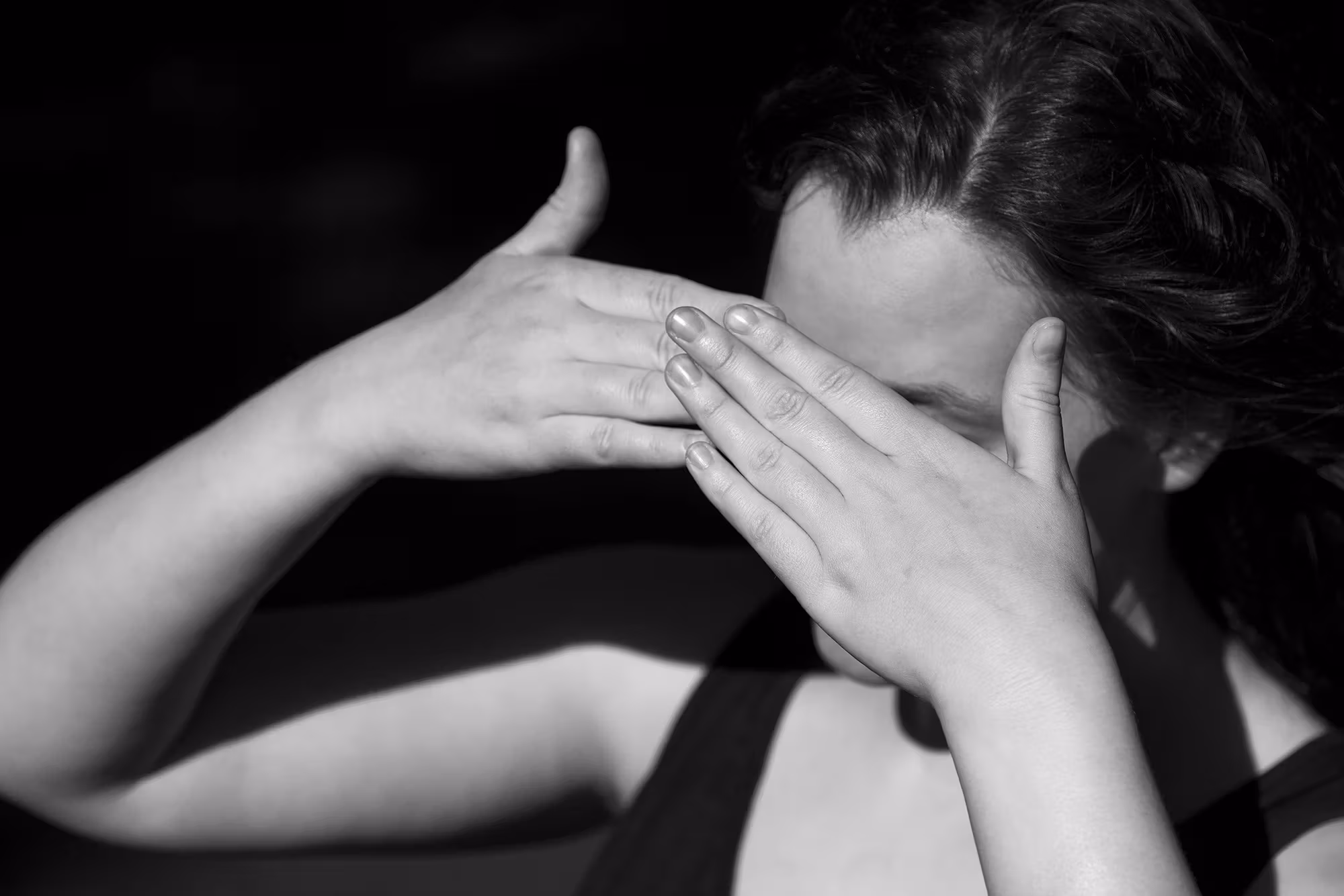 A photograph of an individual covering their eyes as if the sun was shining into them. 