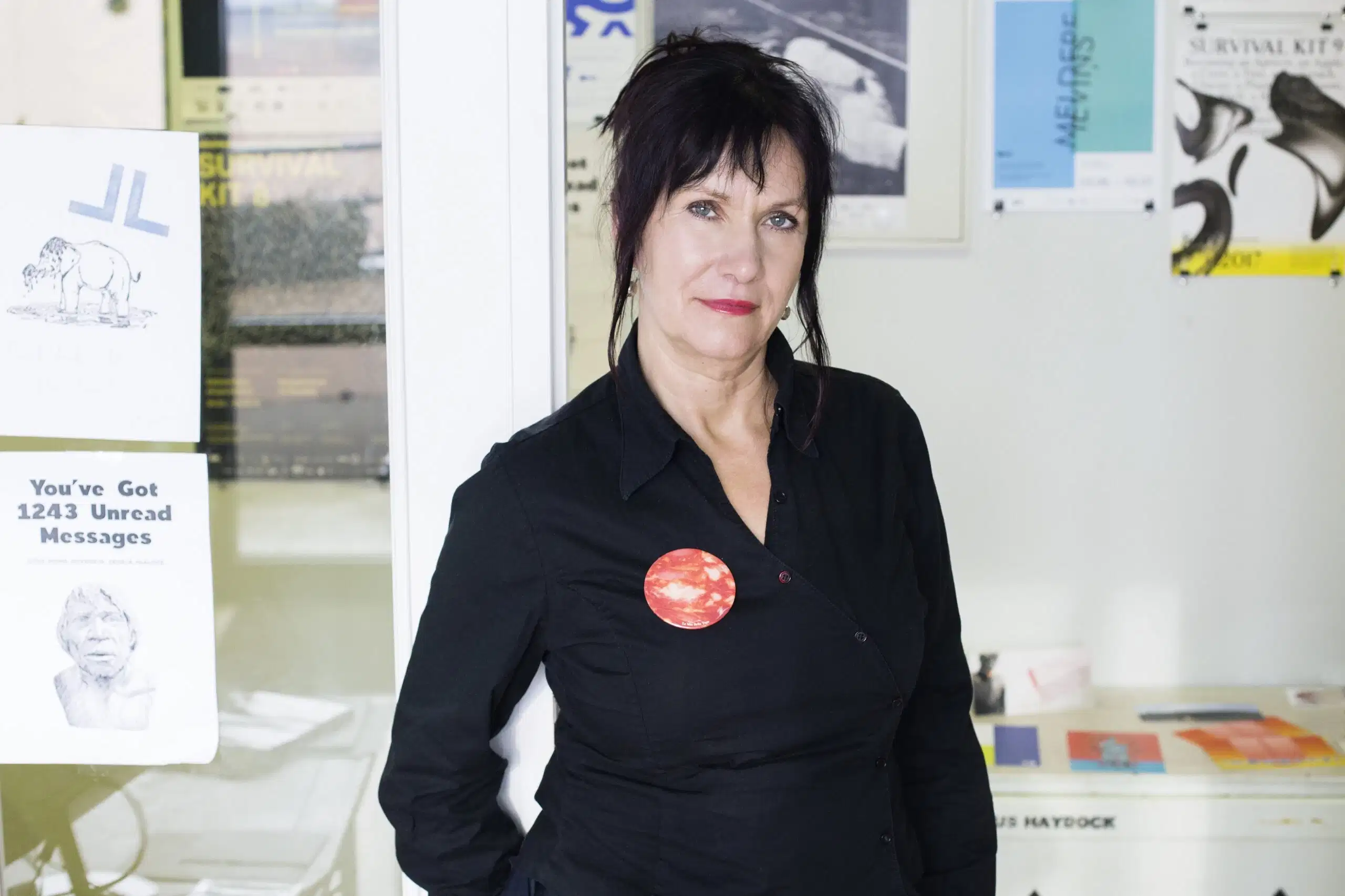 A person in a black button up shirt with red and blue buttons in white room decorated with posters