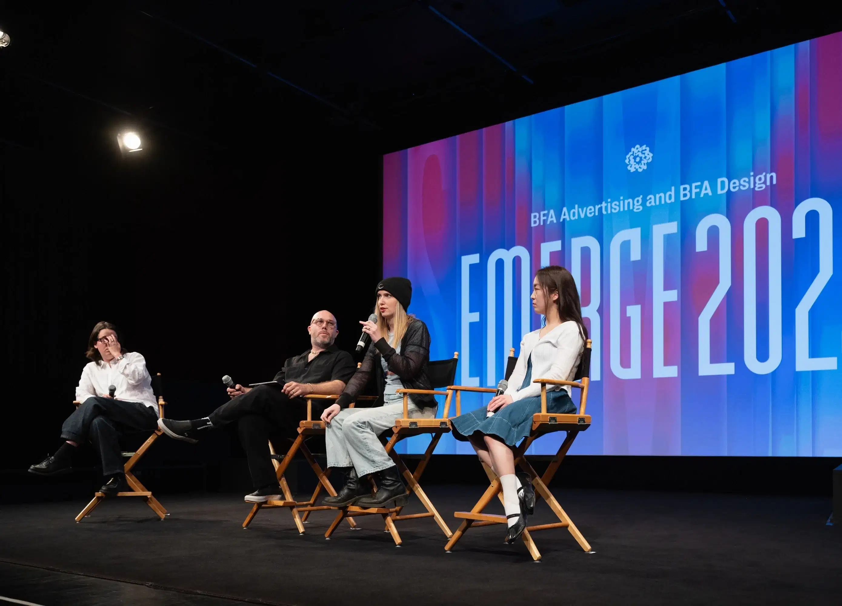 a group of people sit on a stage in front of a screen that reads "EMERGE"