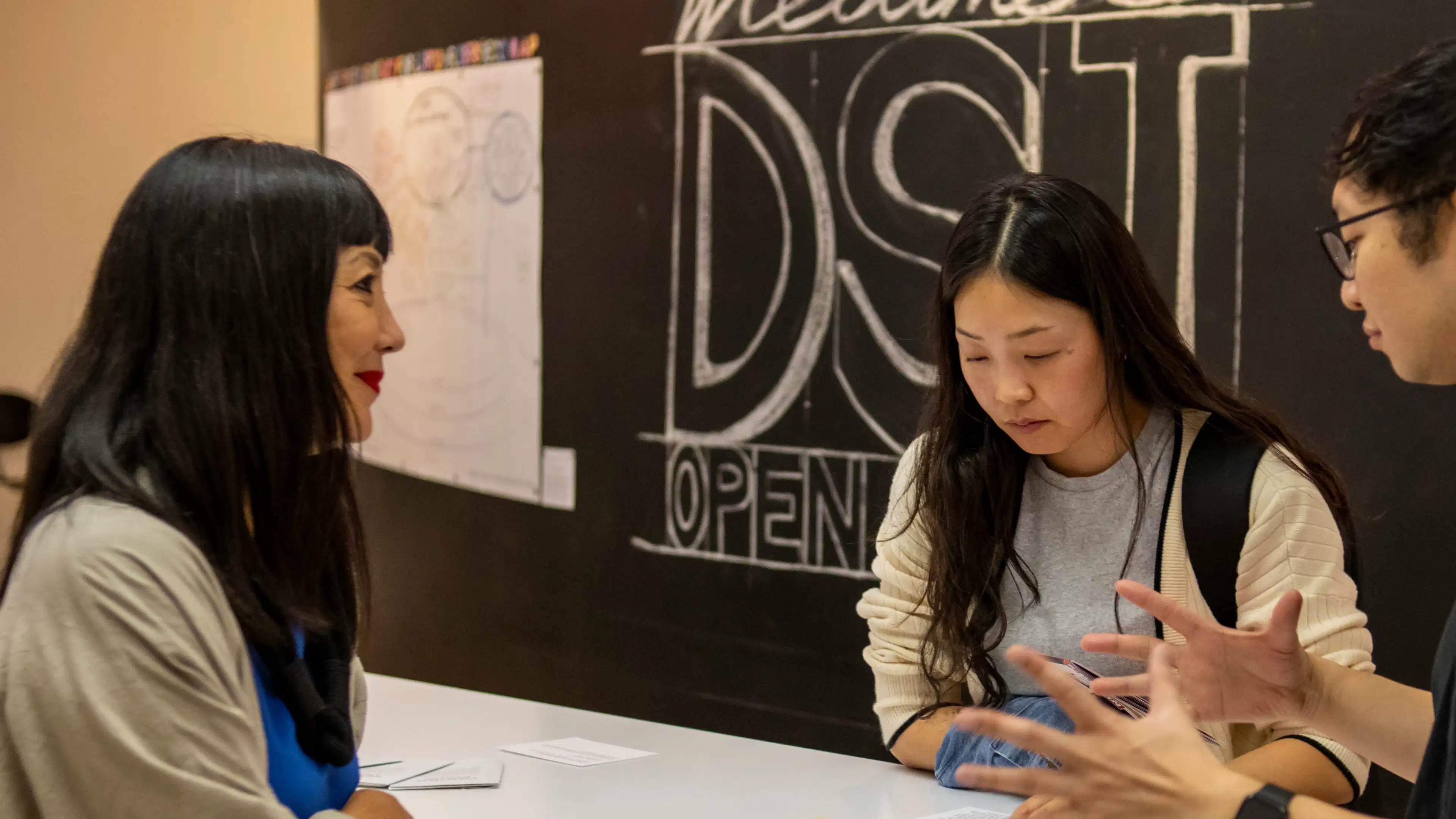 a person with long dark hair on the left looking at 2 students speaking.