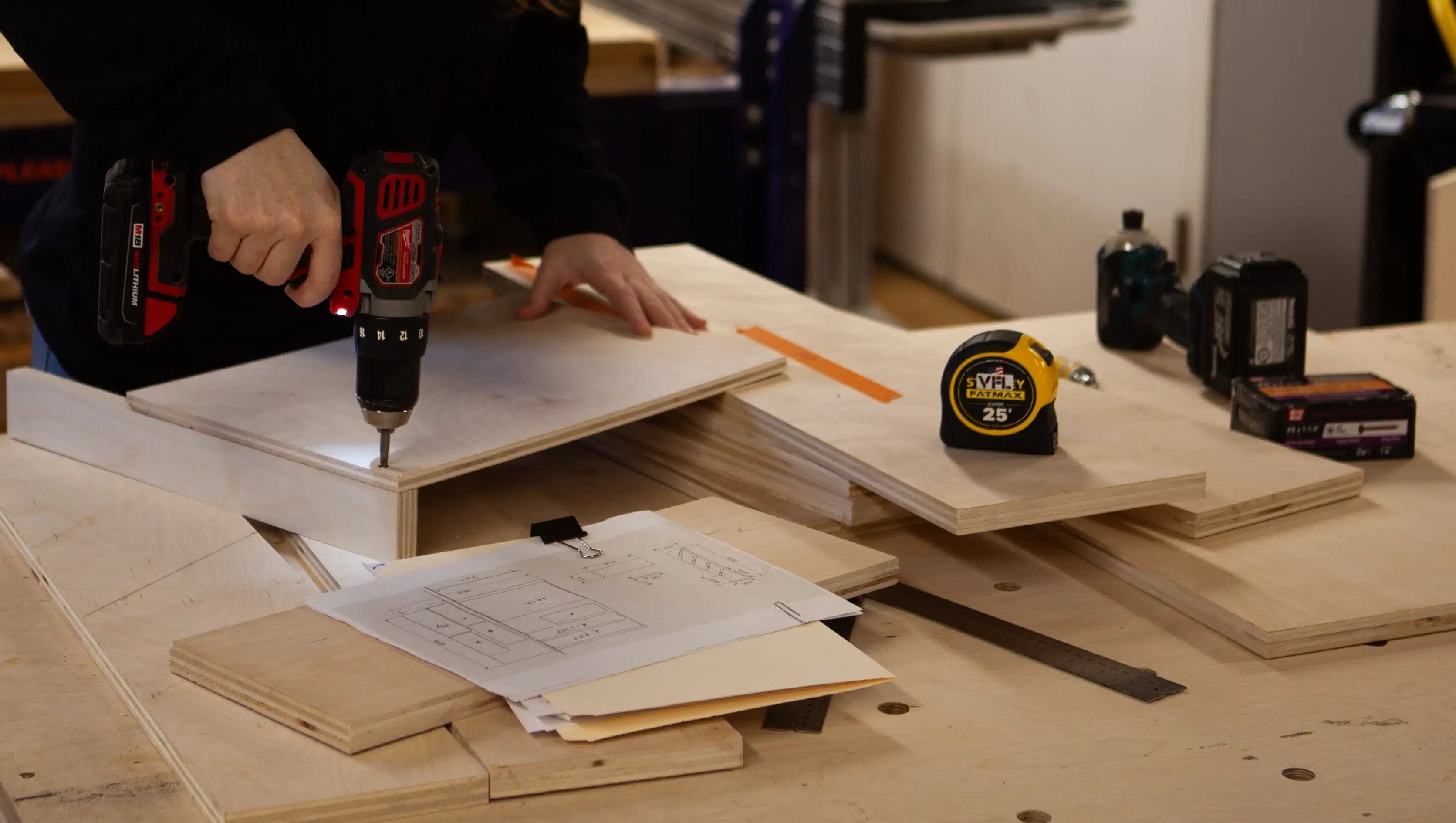 Wide photo of person inserting screws into plywood; shop drawing in foreground