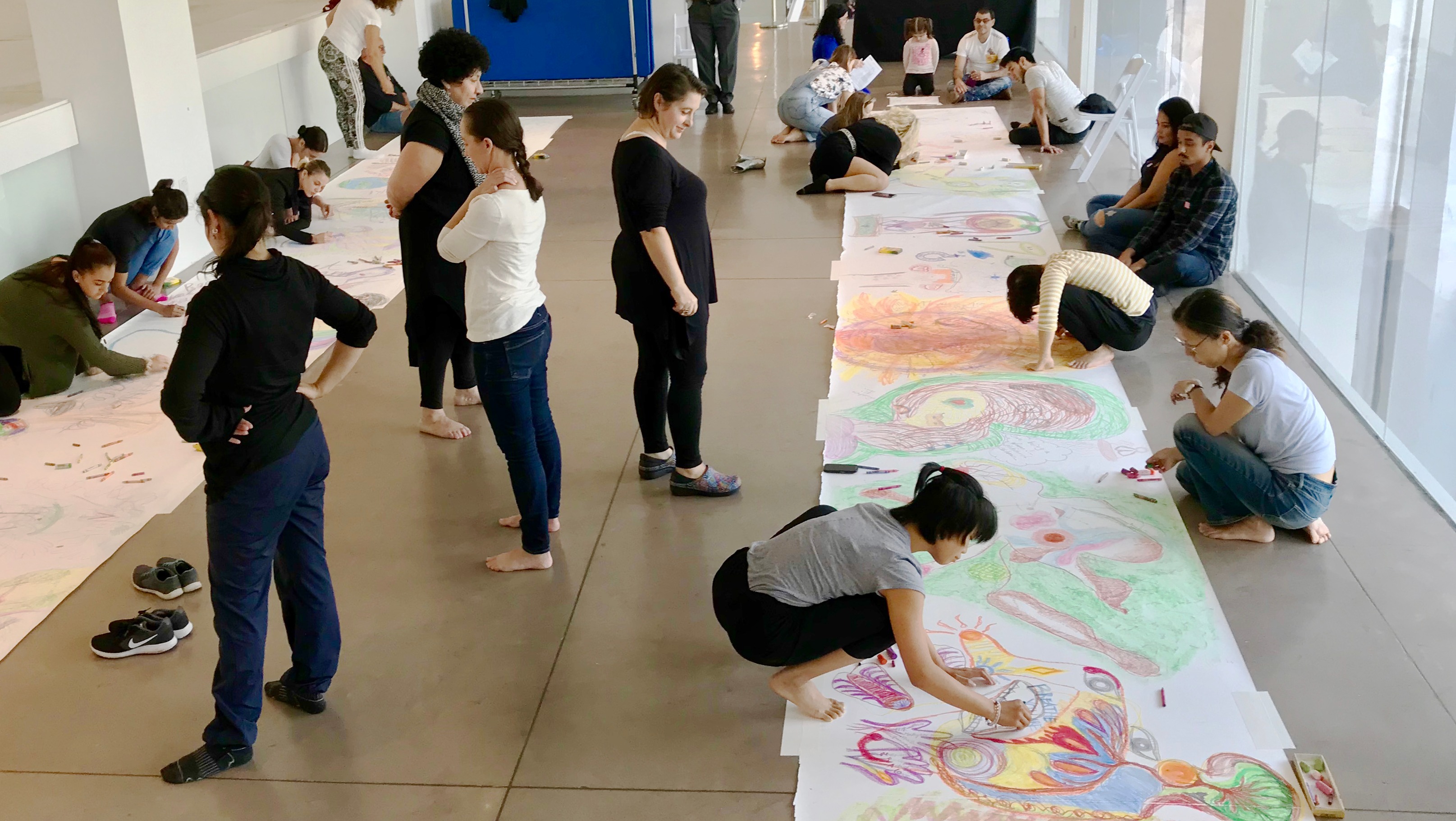 a room full of students drawing on a roll of paper on the floor.