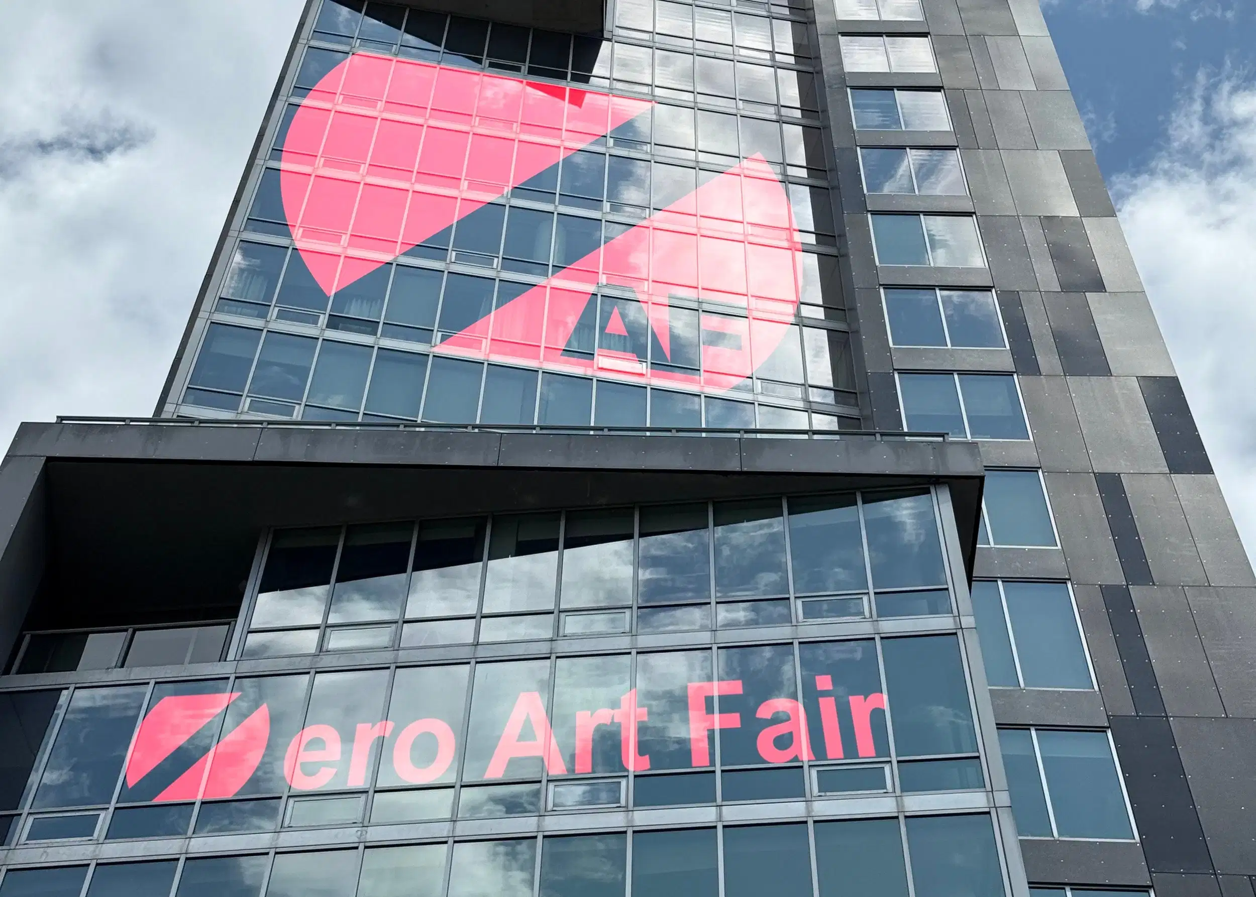 A modern skyscraper facade with the Zero Art Fair logo displayed in its windows.