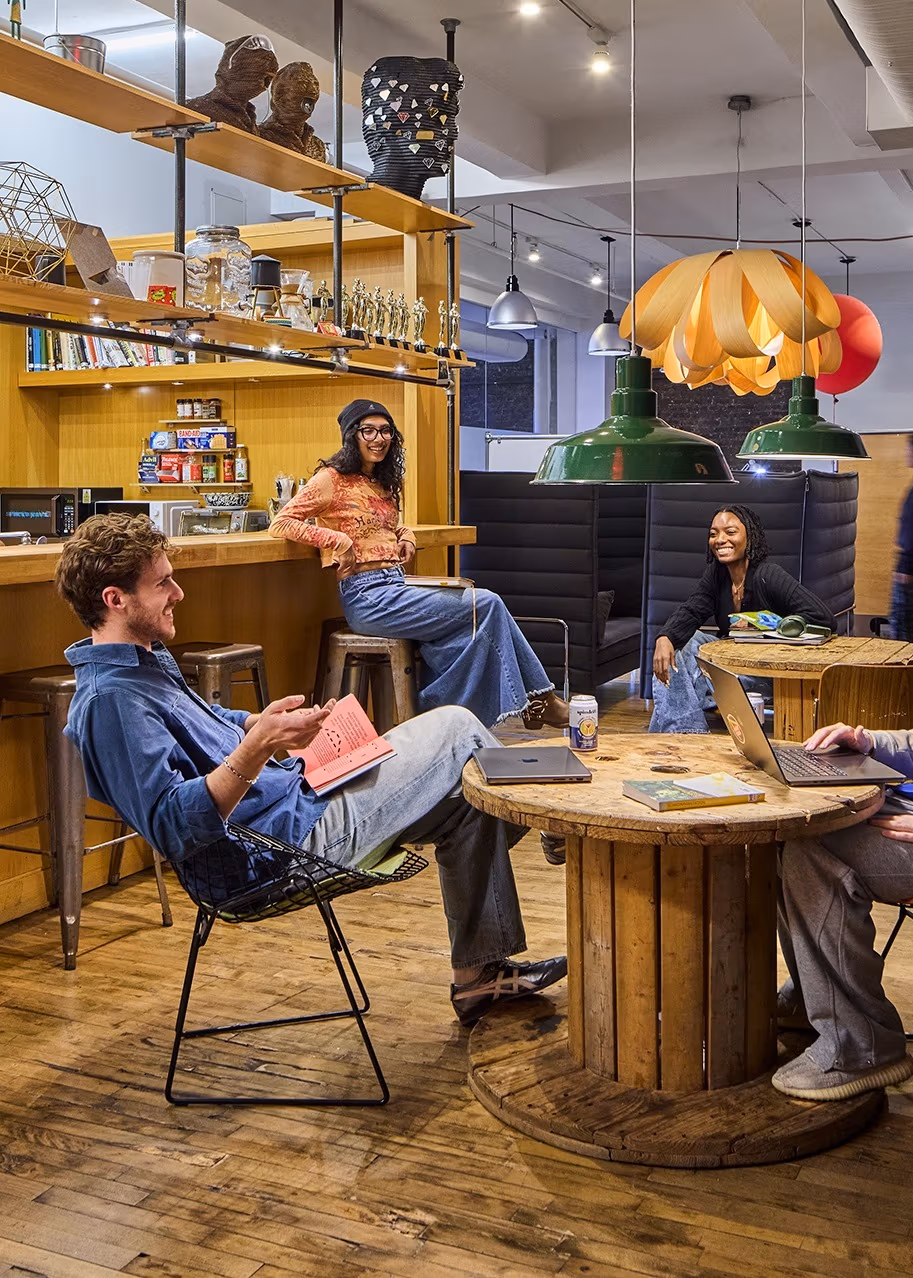 Four students exchange ideas while studying together in lounge area with laptops, books.