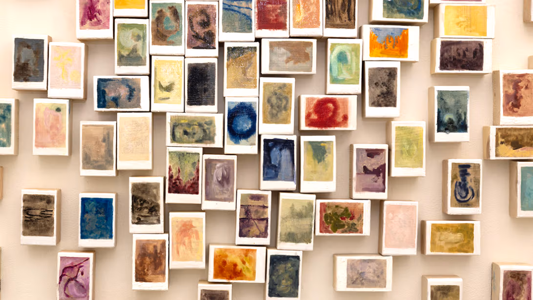 Wall of 50+ multiple three-dimensional color oil abstract paintings with white boarders characteristic of polaroid photographs.