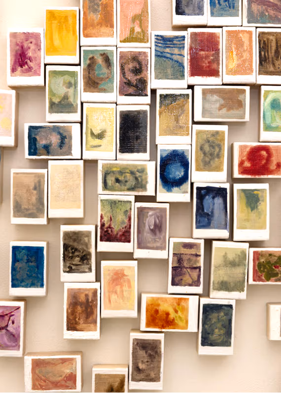 Wall of 50+ multiple three-dimensional color oil abstract paintings with white boarders characteristic of polaroid photographs.