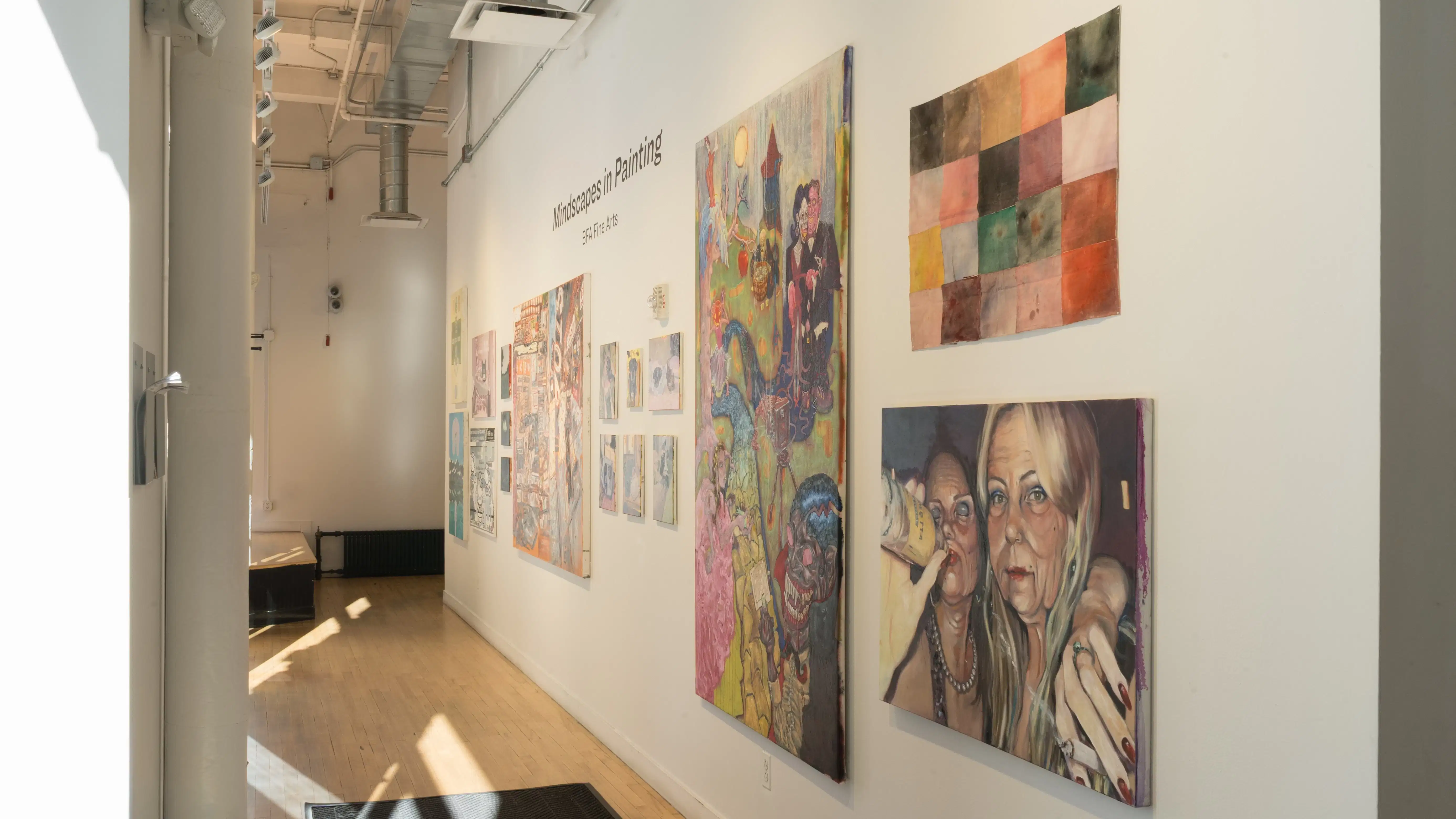 A long gallery wall displays paintings by several different artists, ranging from small to oversized.