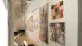 A long gallery wall displays paintings by several different artists, ranging from small to oversized.