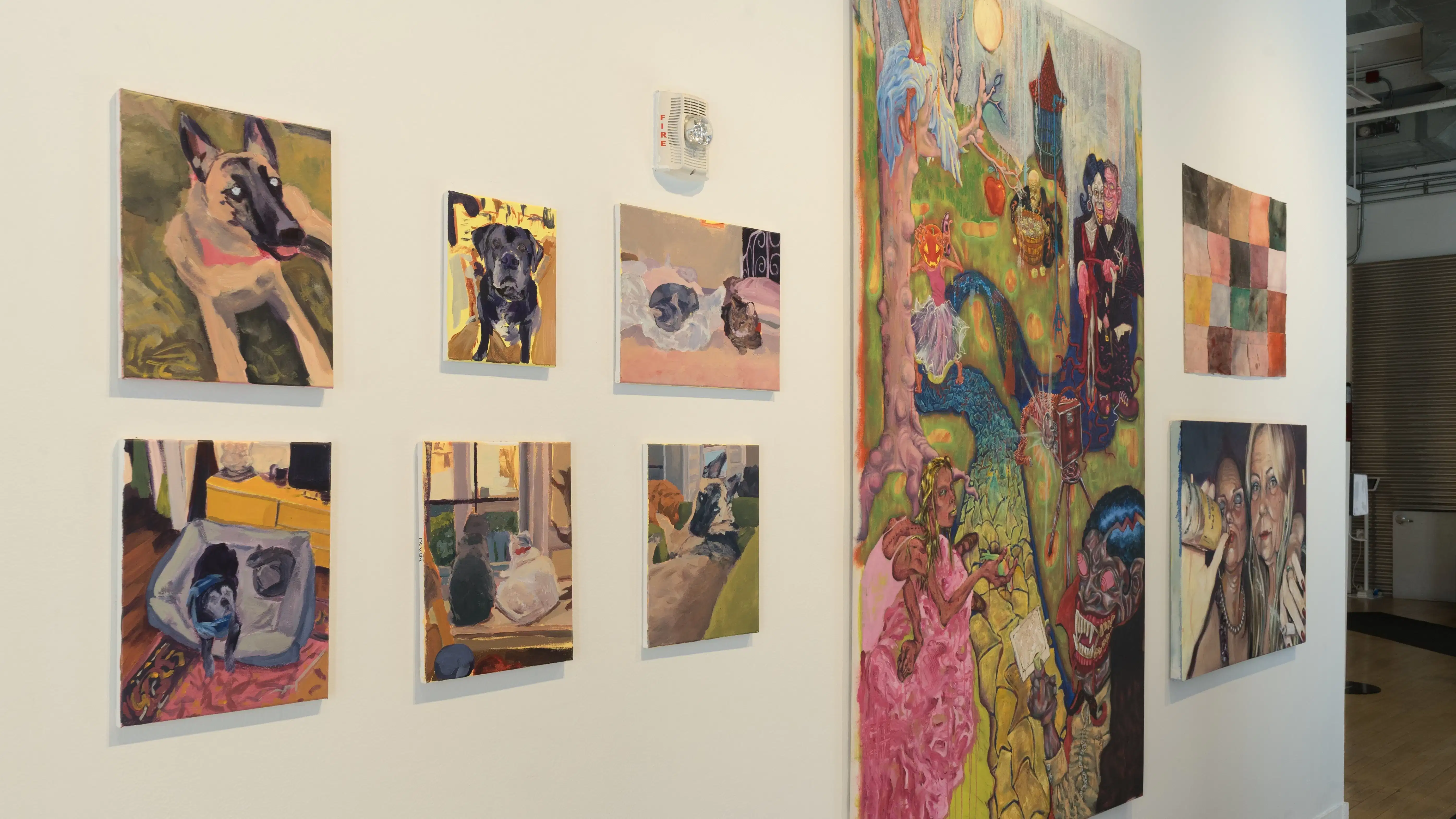 A row of paintings on a gallery wall in many different sizes, ranging from abstract to figurative.