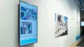 A vertically-installed screen showing Paulaine Lockward's "Harvesting Hope" project, with 3D renderings of a hotel space and text about the intention below them. To the right is a vinyl print of another 3D-rendered environment (no attribution). 