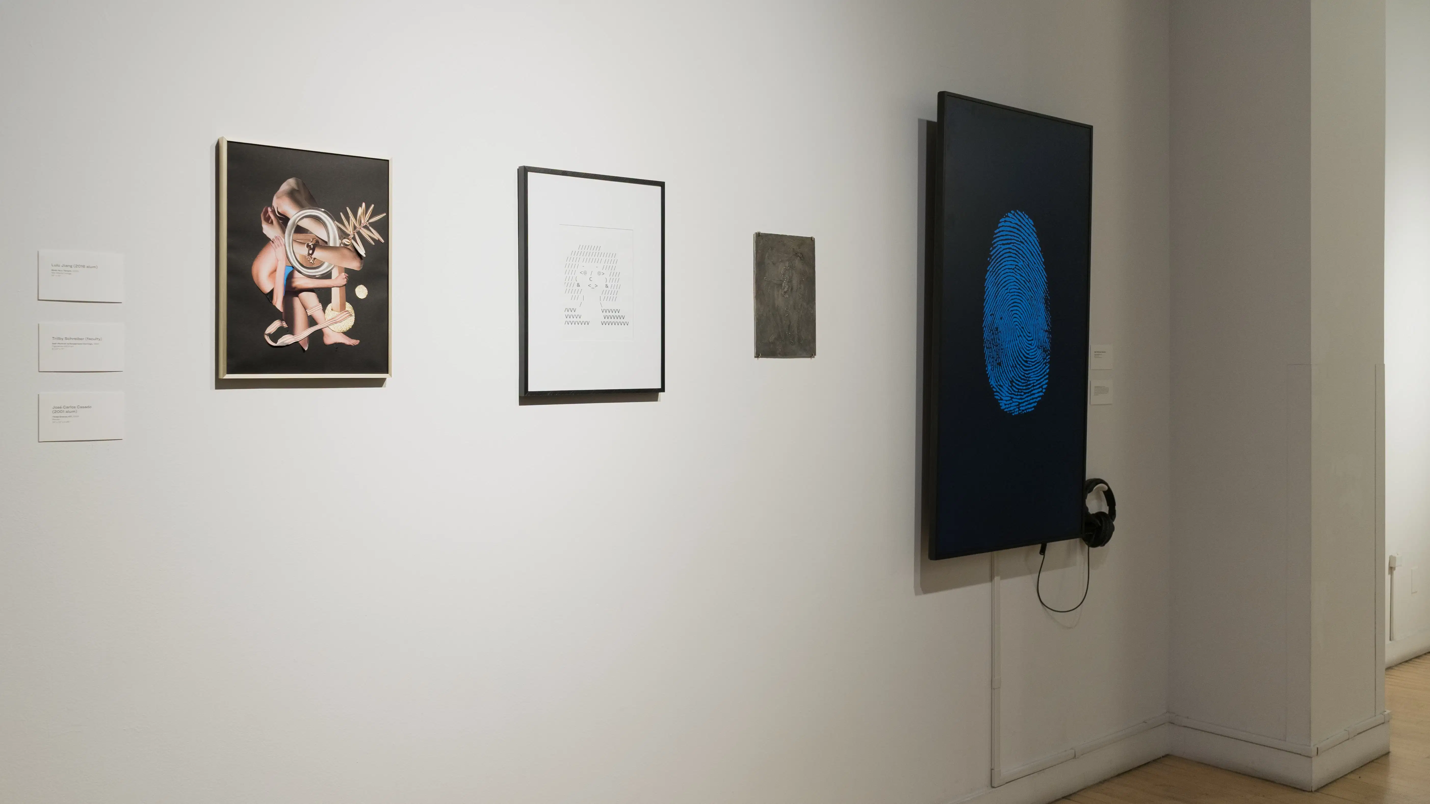 Continuing into the other hallway, two framed works are displayed next to a small, dark, unframed work. To the right of them, a monitor displays a large blue fingerprint.