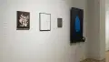 Continuing into the other hallway, two framed works are displayed next to a small, dark, unframed work. To the right of them, a monitor displays a large blue fingerprint.