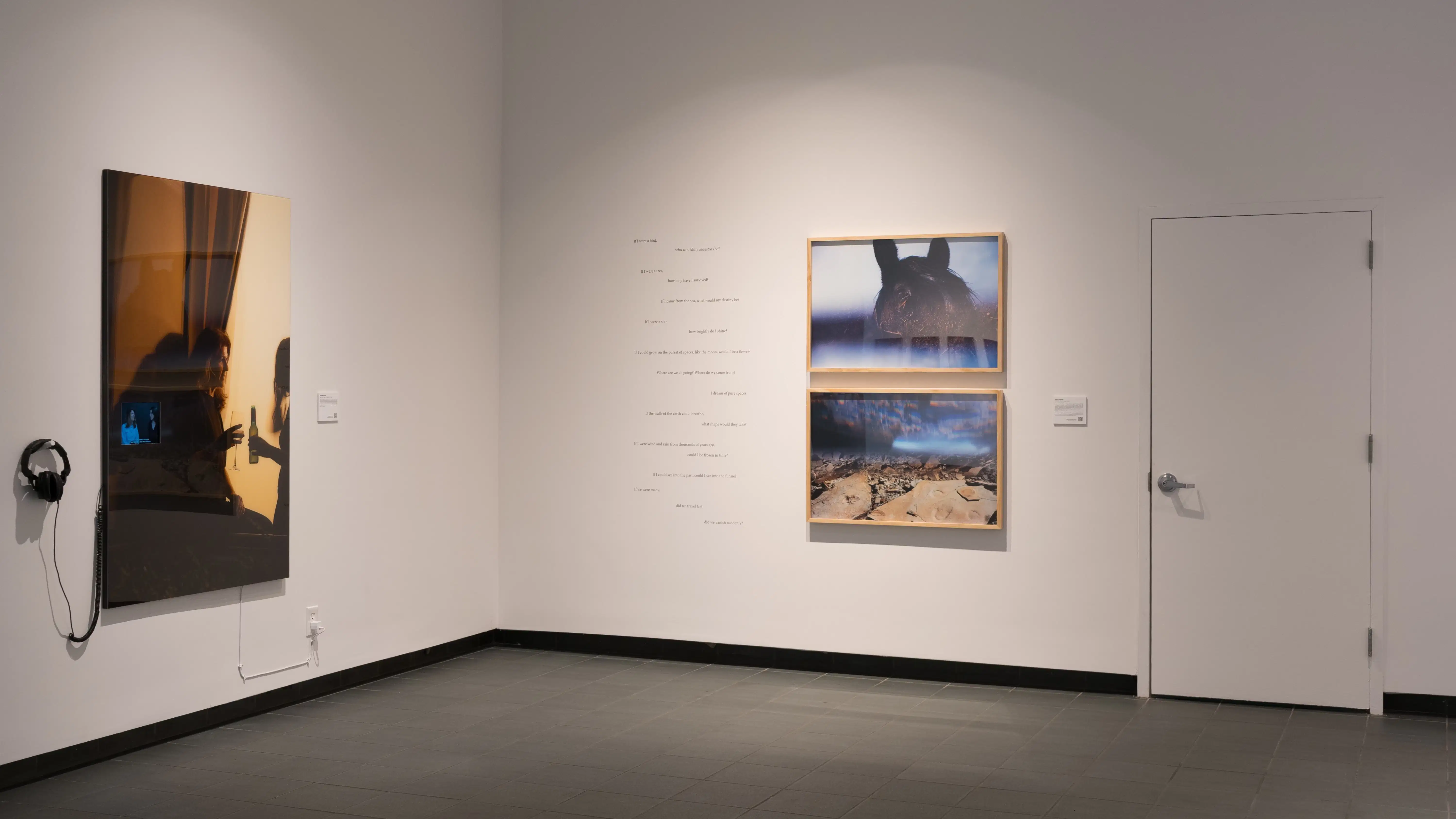A corner wall in SVA’s Gramercy Gallery with one image on the left with headphones resting beside it, and two photos on the right, with text written on the wall beside it.