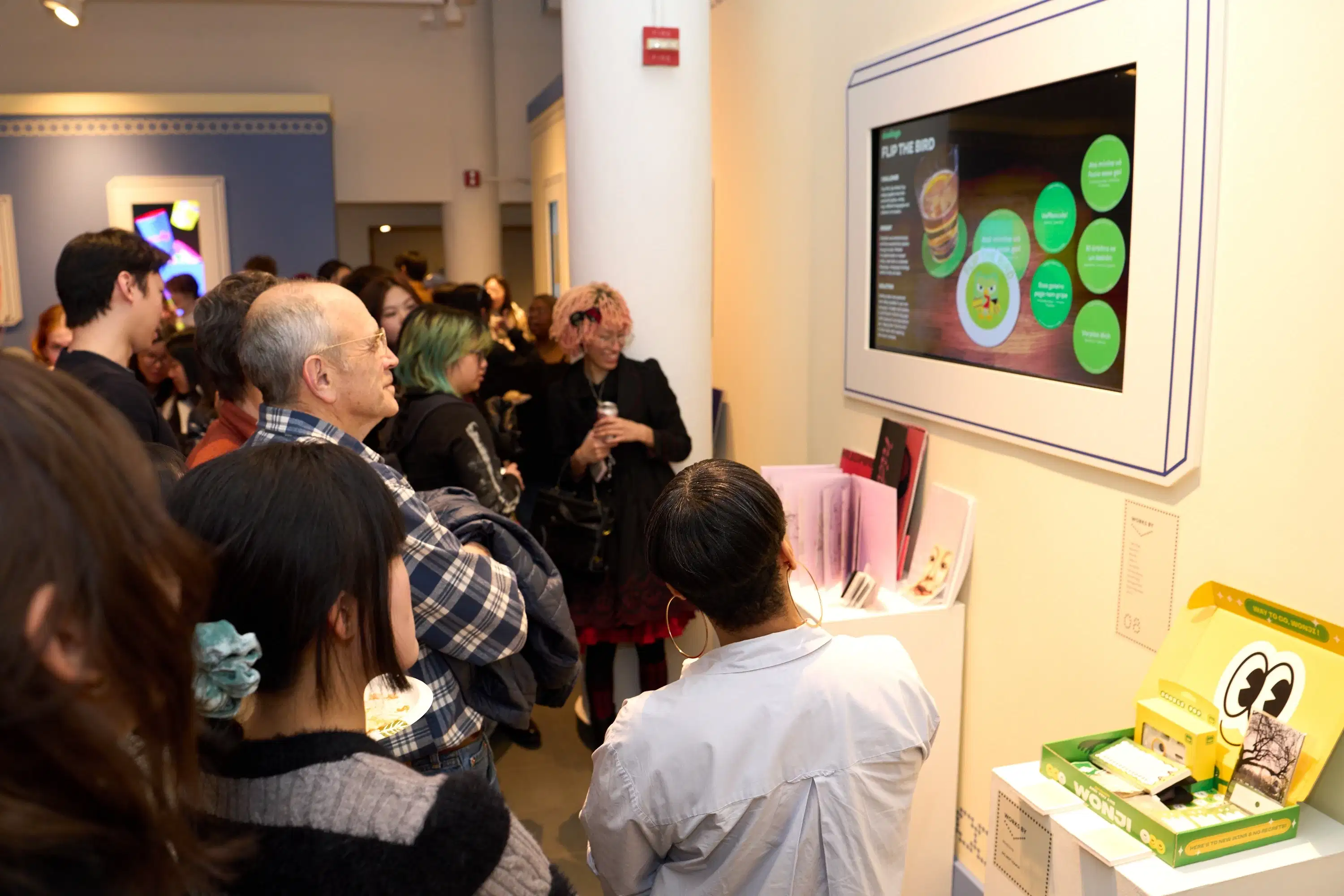 Guests at the opening reception of the annual spring gallery show admire a screen of rotating student advertising work.