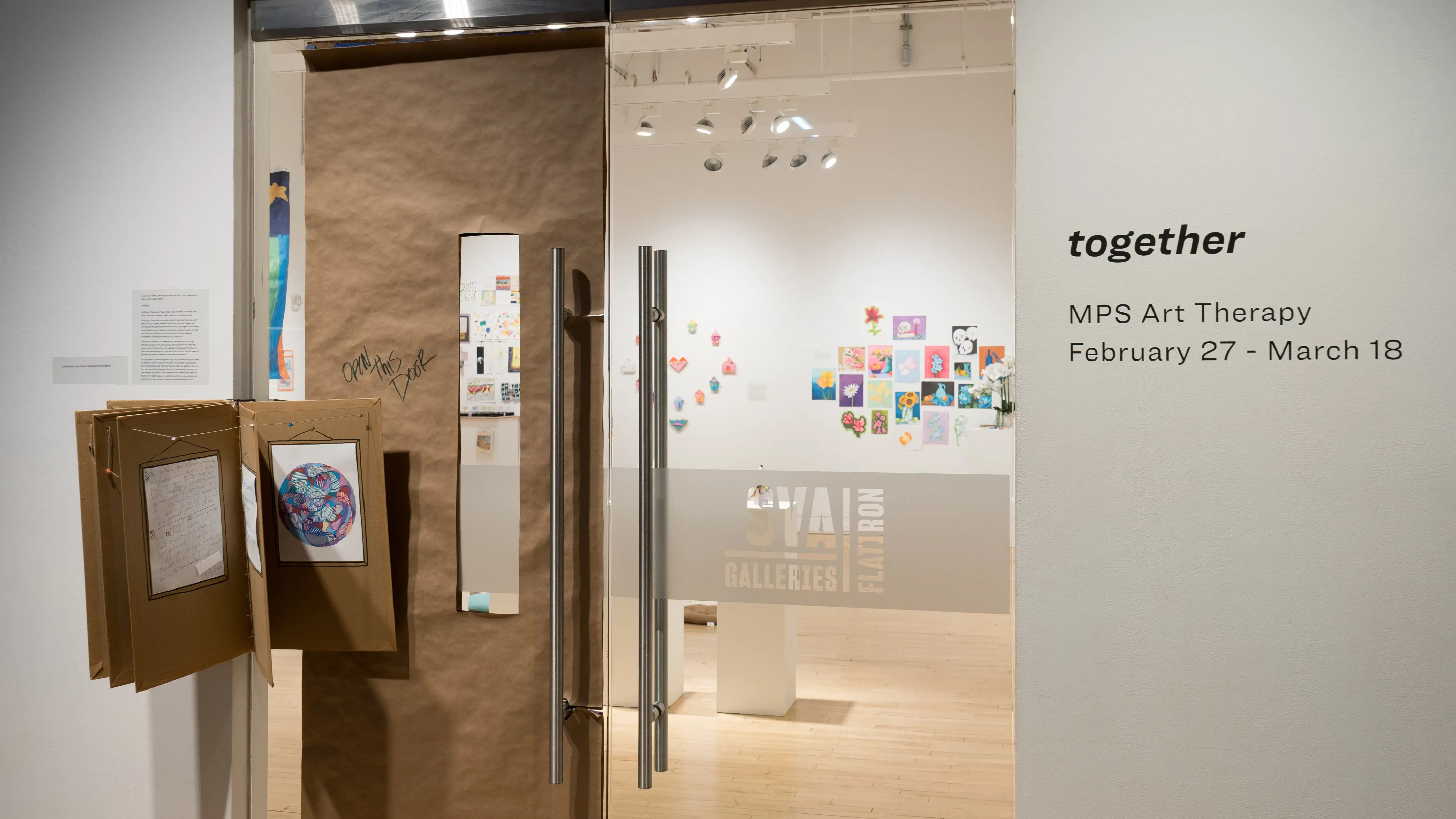 Outside the gallery, the exhibition title is displayed in vinyl to the right of the door. The left half of the glass door is covered with kraft paper, and an accordion-like structure is attached to the hinge side.
