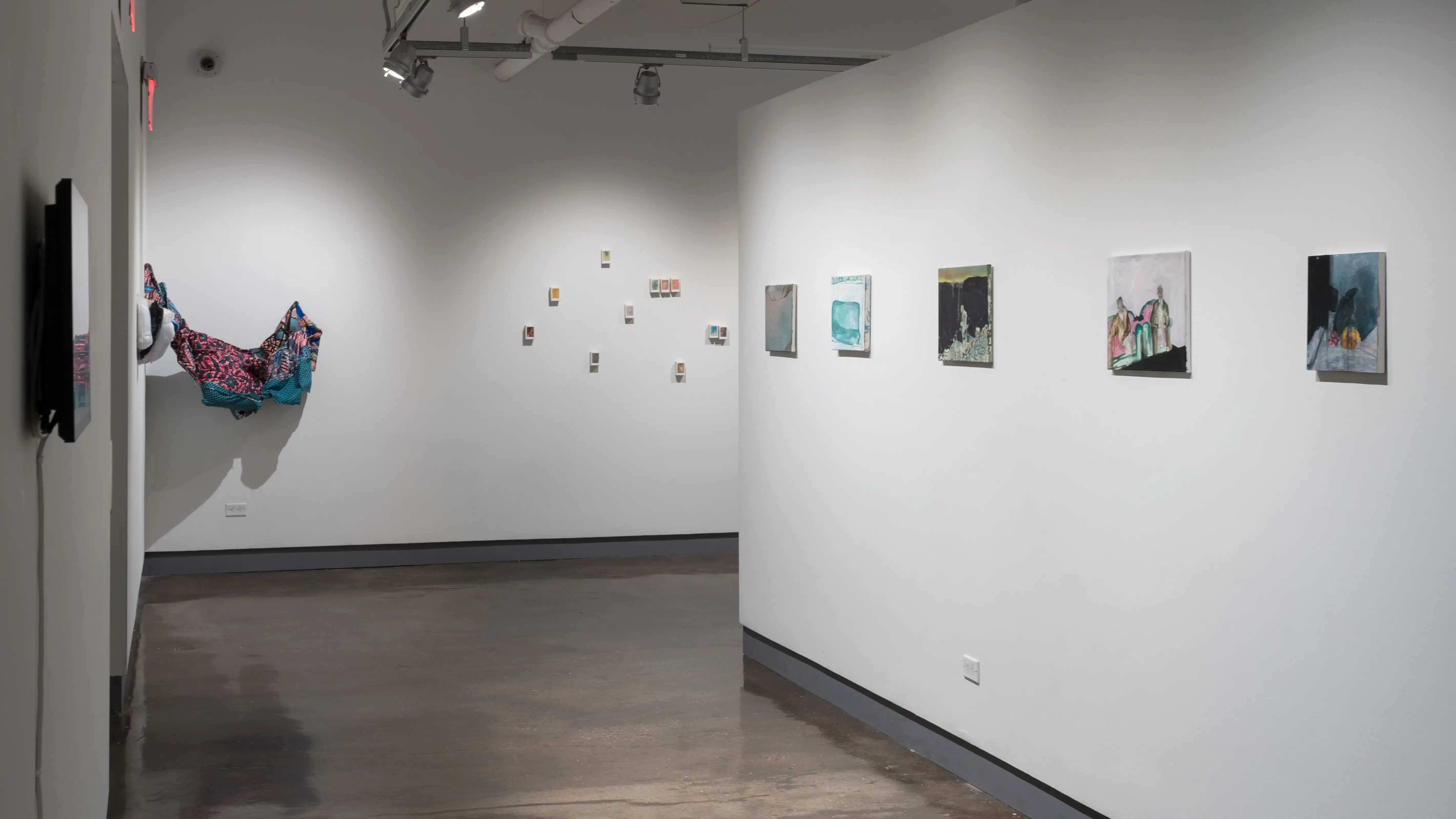 Into the hallway of the fourth gallery, a row of paintings hang on the right wall, with more paintings and a mixed media sculpture on the farther wall.