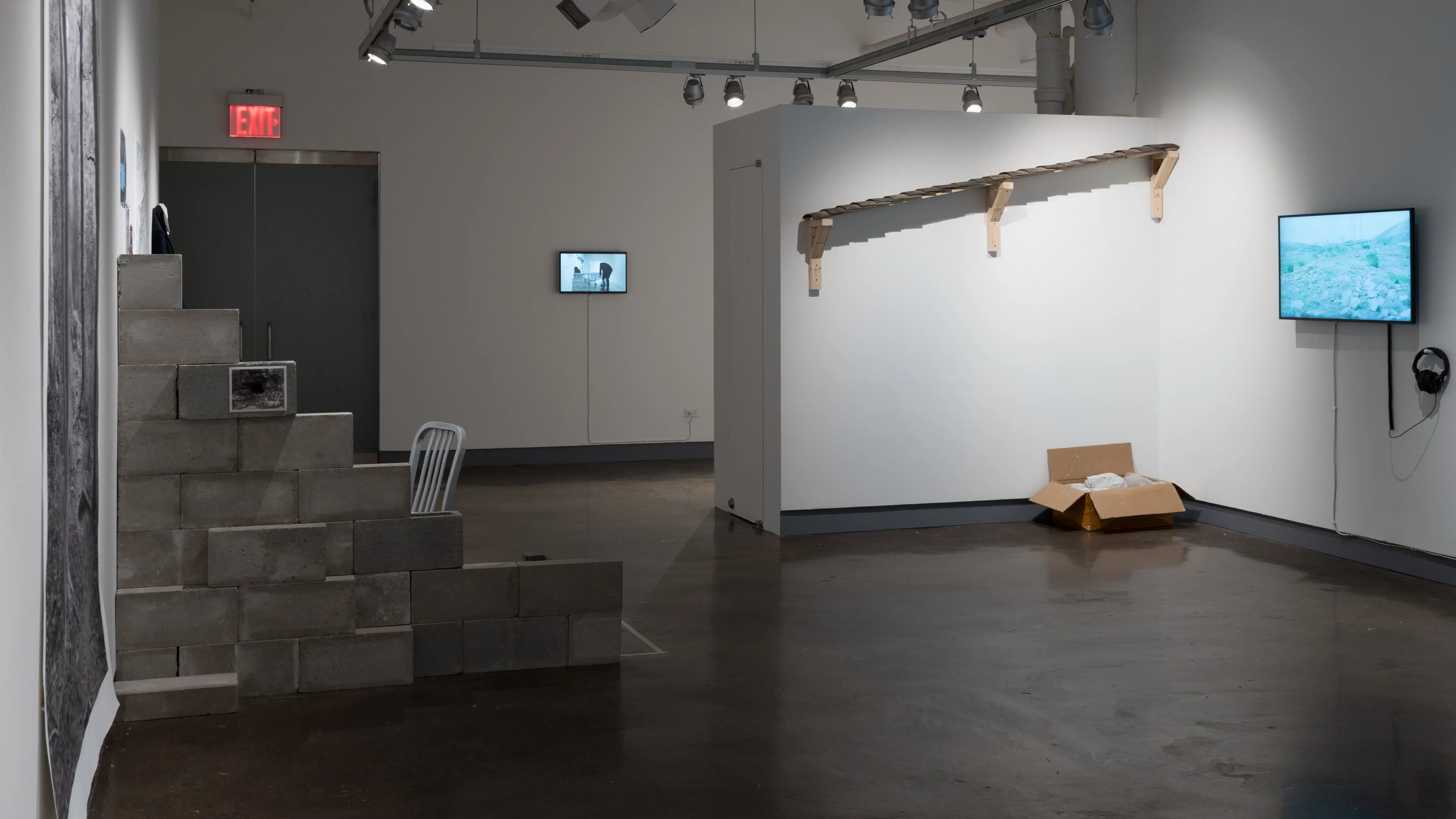 A shot of the third gallery space with several installation pieces including a row of bricks against the left corner.