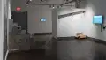 A shot of the third gallery space with several installation pieces including a row of bricks against the left corner.