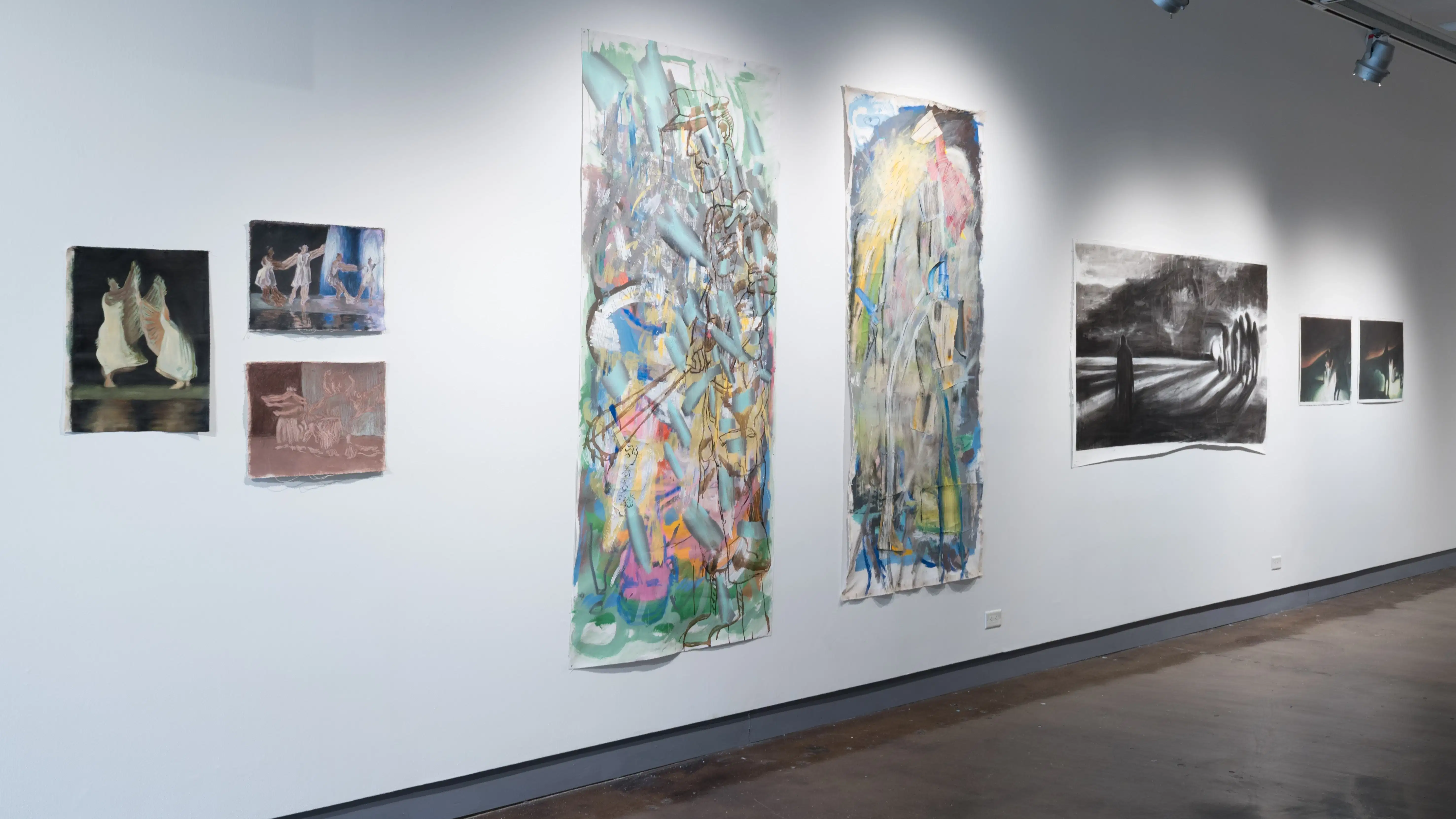 A row of several artworks hangs on the wall, ranging in size and color.