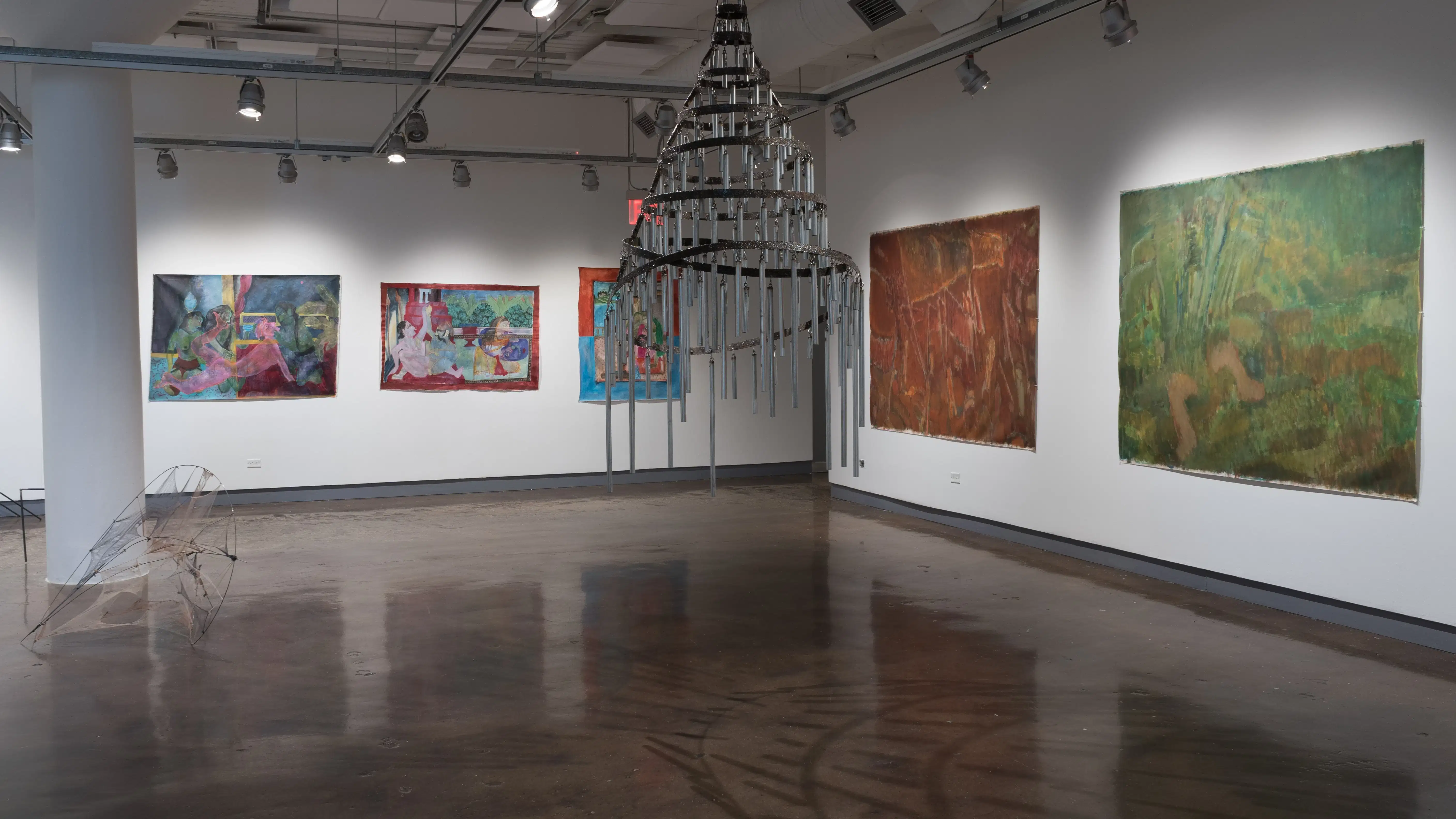 A chandelier-like sculpture hangs in the center of the room, as paintings hang on the two walls behind it.