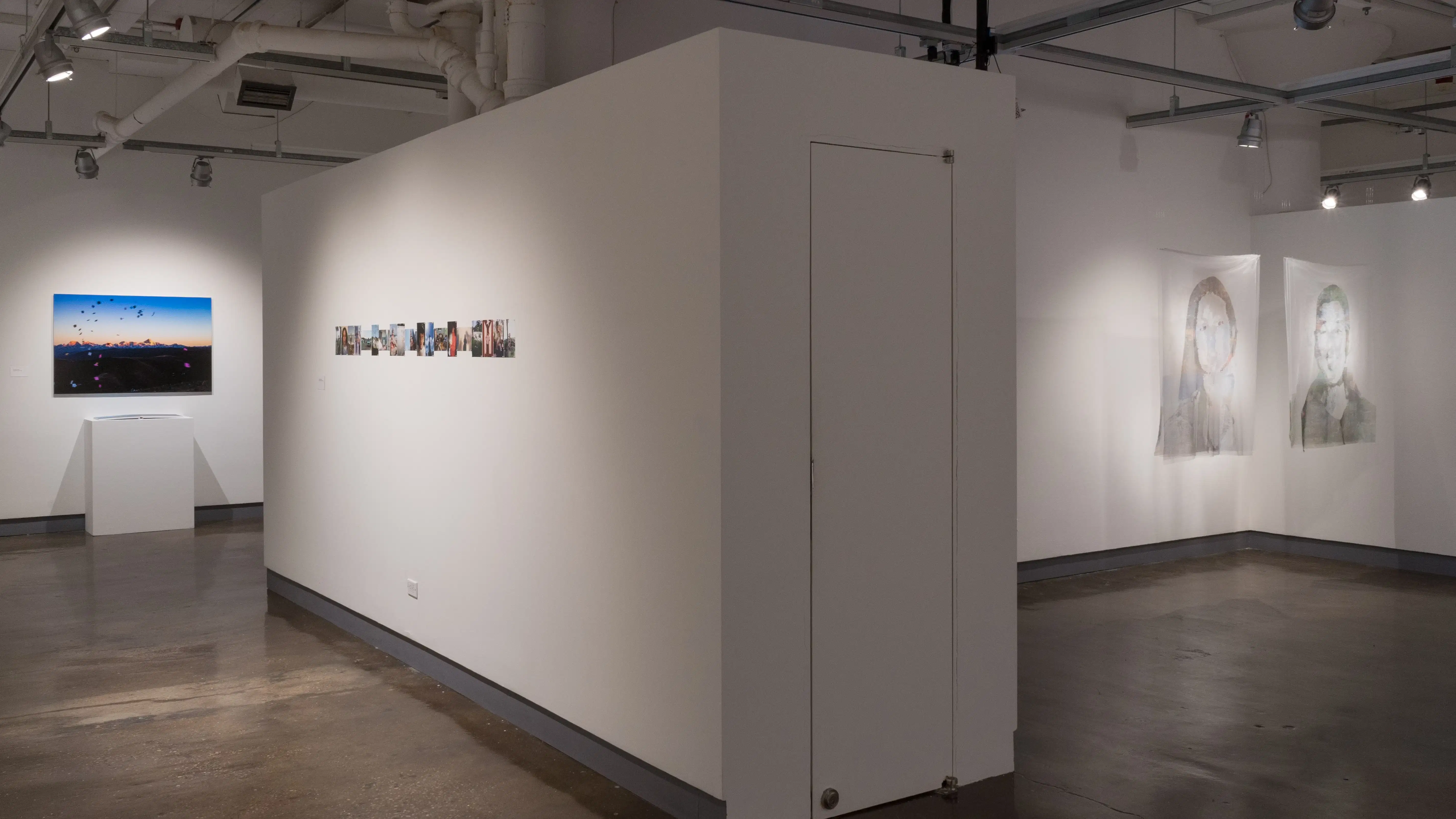 From the corner in gallery three, a large photograph in gallery four is visible, as well as a row of small photographs in the left hallway. In the alcove of gallery three, two portraits on fabric are suspended from the ceiling.