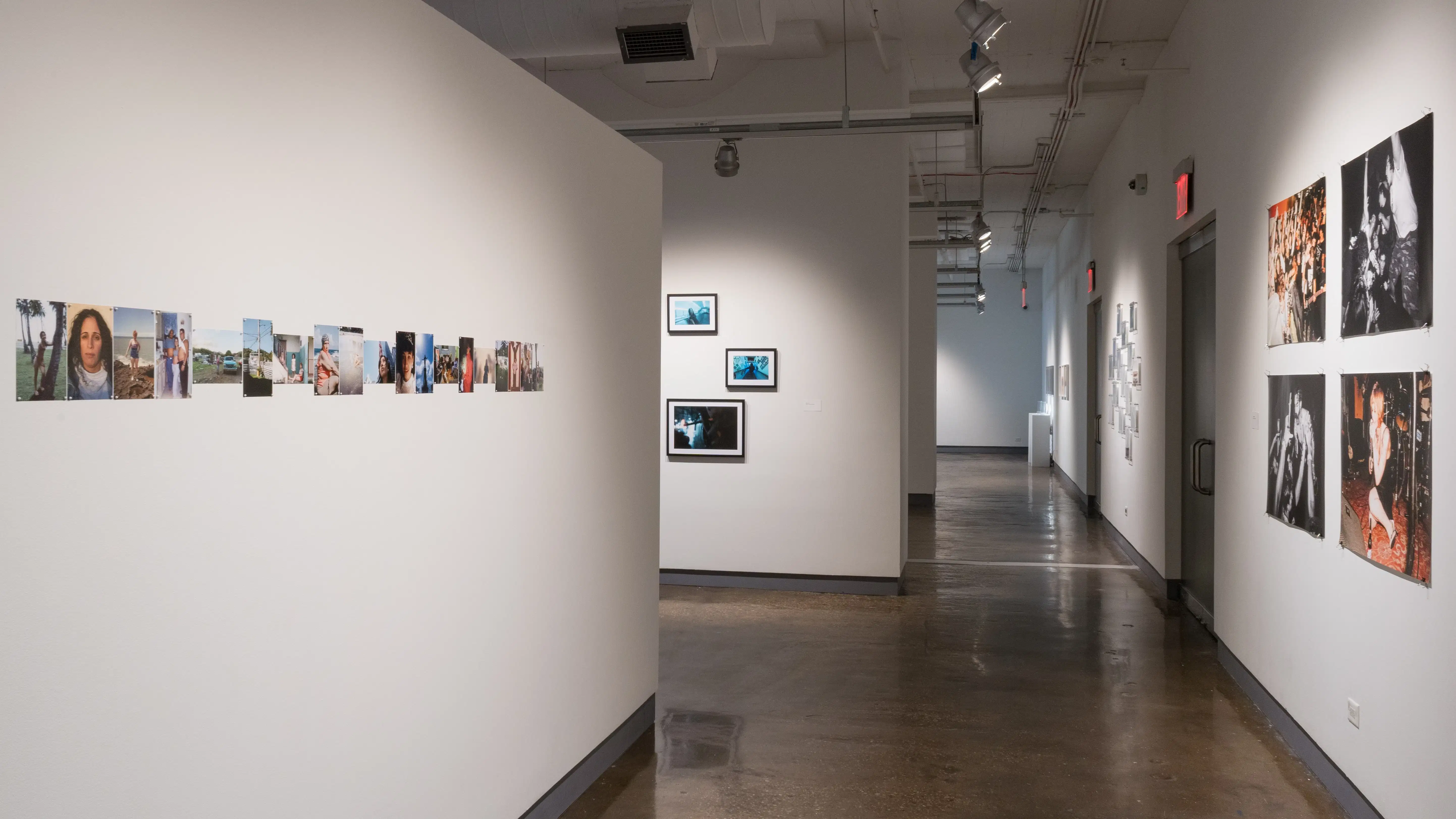 Looking down the gallery’s left hallway, a series of small photographs is arranged in a row on the left wall. On the right, a grid of four large photographs from a concert. Works in galleries one, two, and three are visible further down the hall.