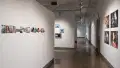 Looking down the gallery’s left hallway, a series of small photographs is arranged in a row on the left wall. On the right, a grid of four large photographs from a concert. Works in galleries one, two, and three are visible further down the hall.